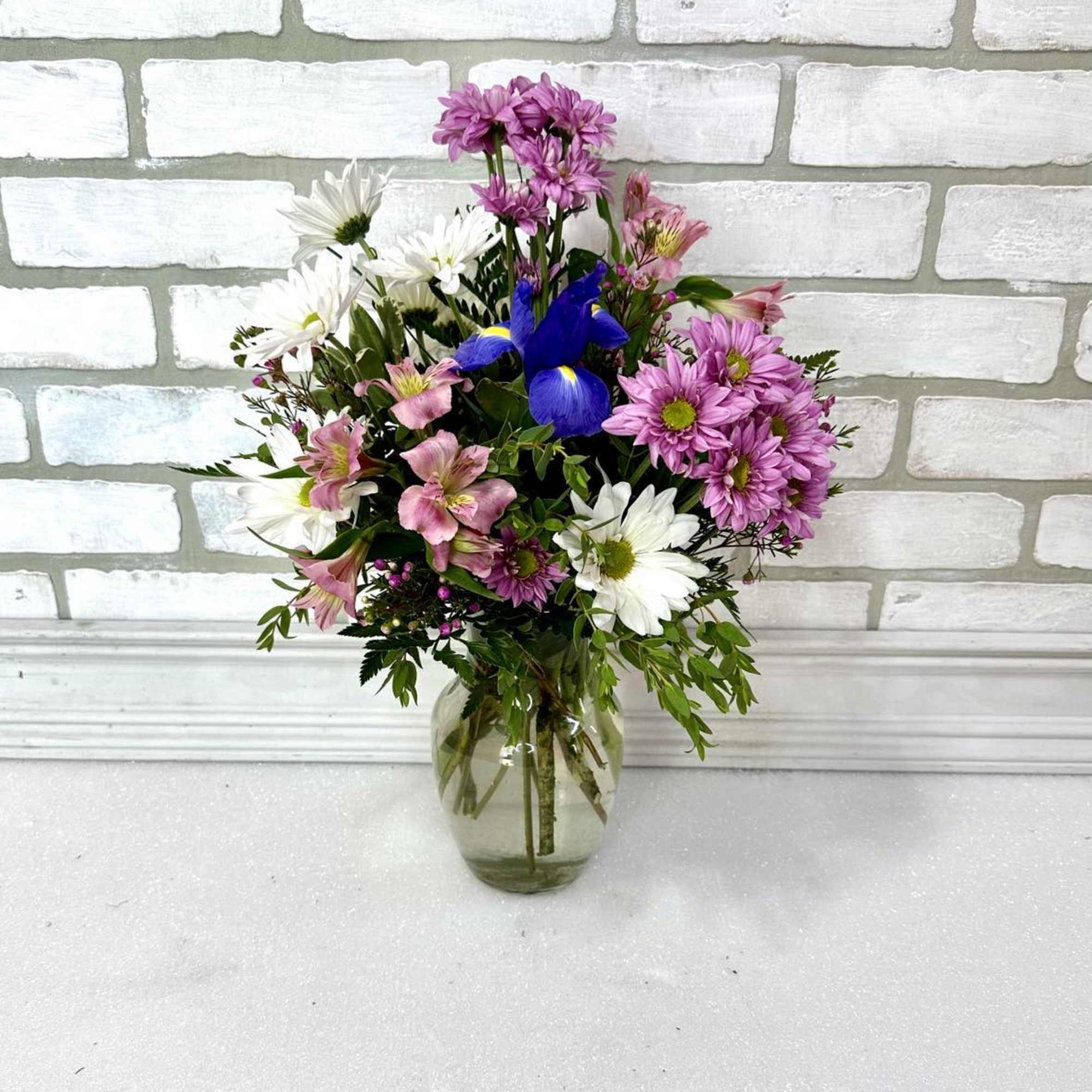Mixed bouquet of pink, white, and blue flowers in a clear glass vase