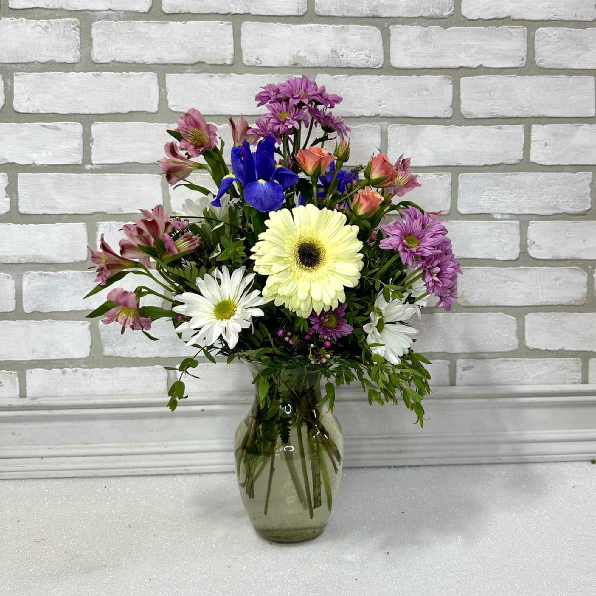 Mixed bouquet of daisies, iris, and pink flowers in a glass vase
