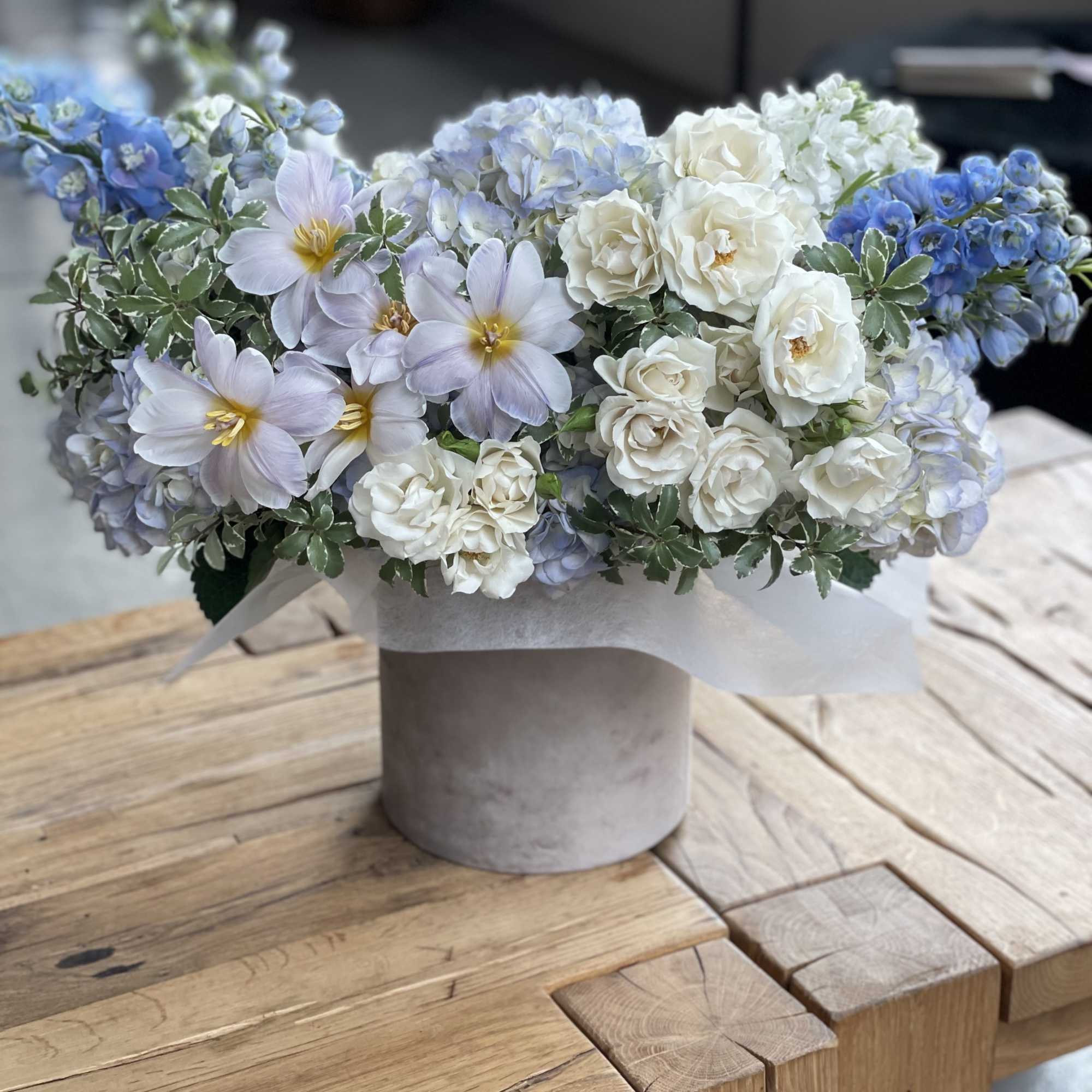 Blue and white floral arrangement in a gray hatbox-style container