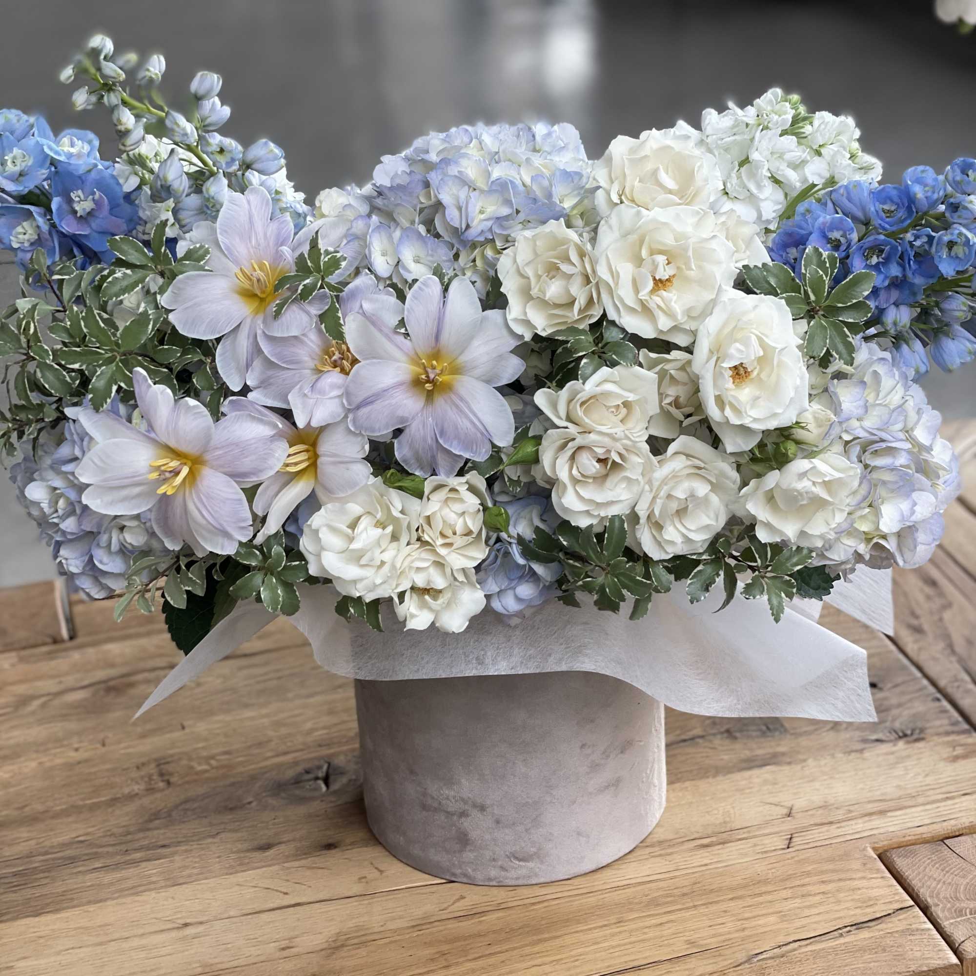 Blue and white flower arrangement in a round gray box