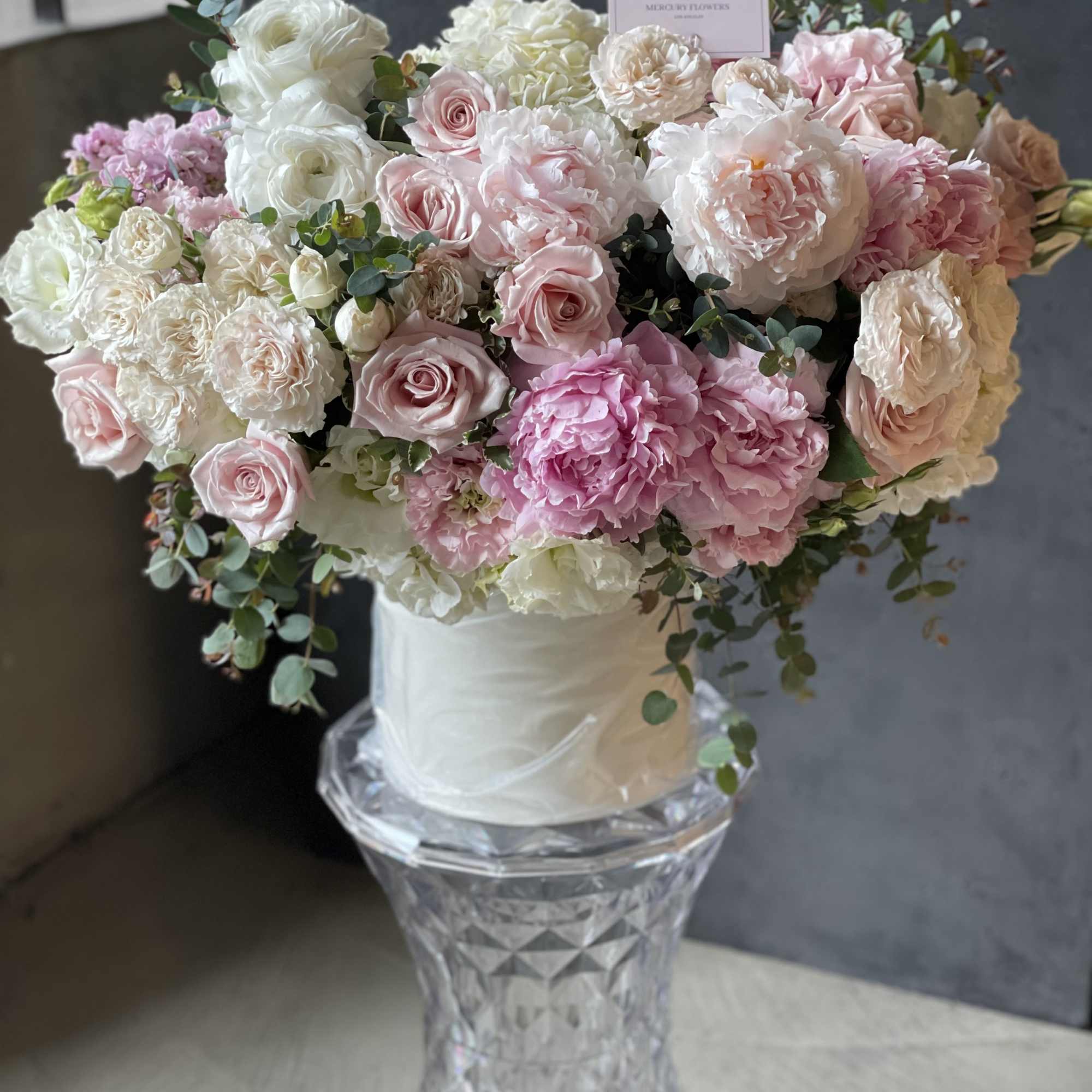 Large bouquet of pink and white roses and peonies in a clear pedestal vase