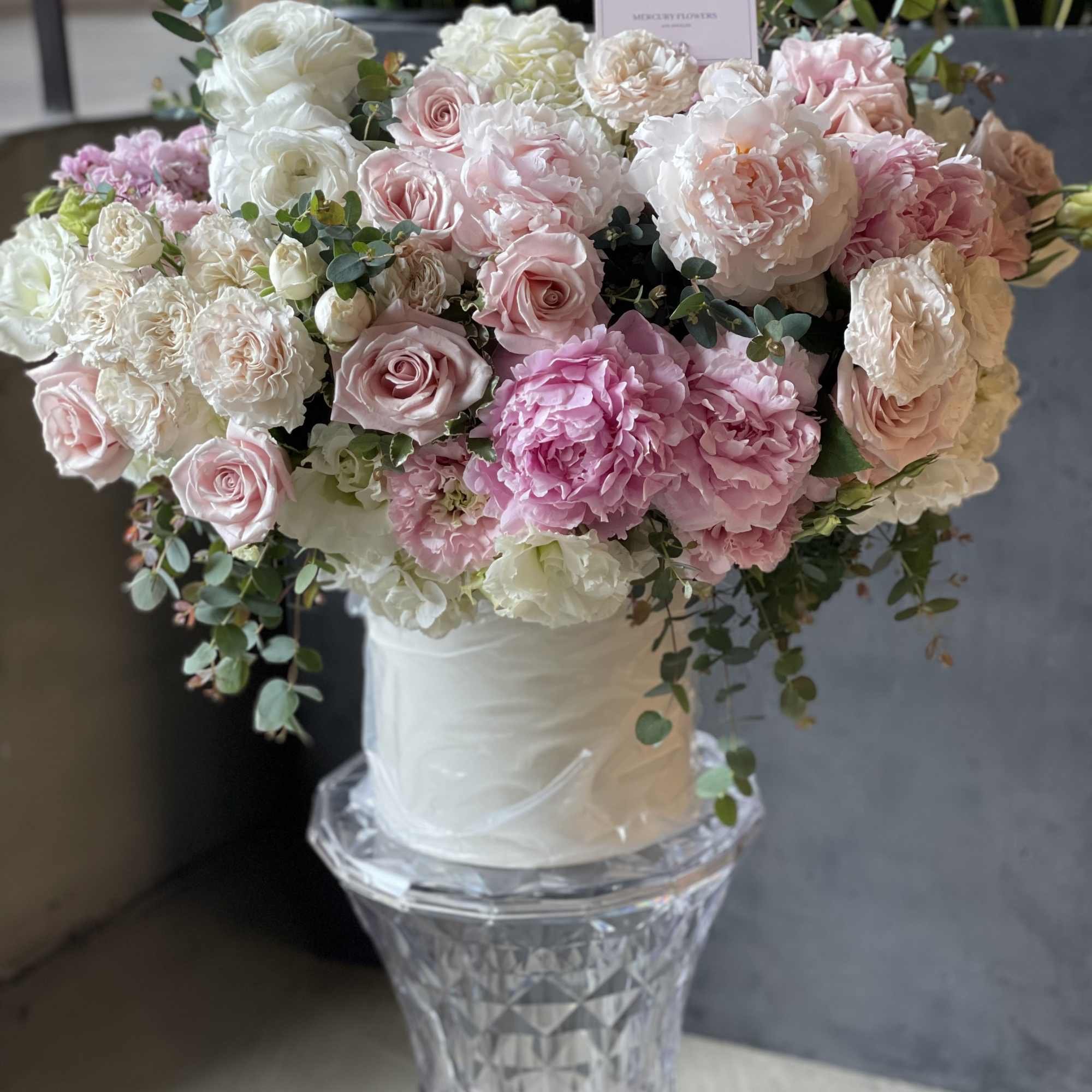 Large bouquet of pink and white roses and peonies in a white hatbox on a glass pedestal