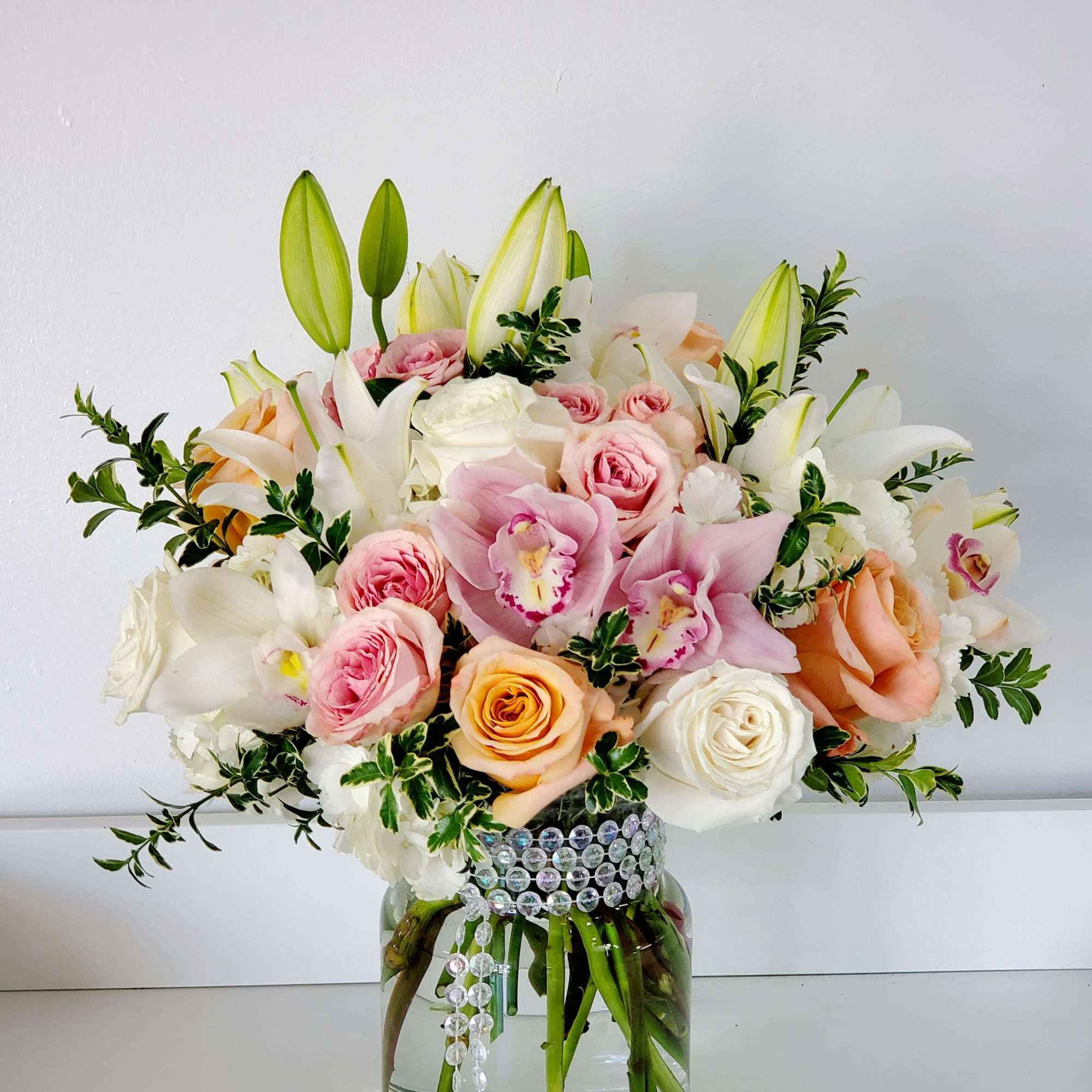 Soft pastel roses, white lilies, and delicate pink orchids come together in