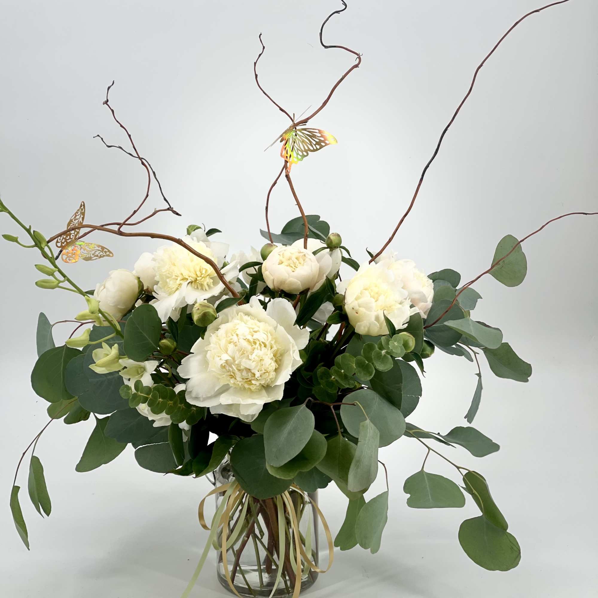 White peony bouquet in a glass vase with curly branches and greenery