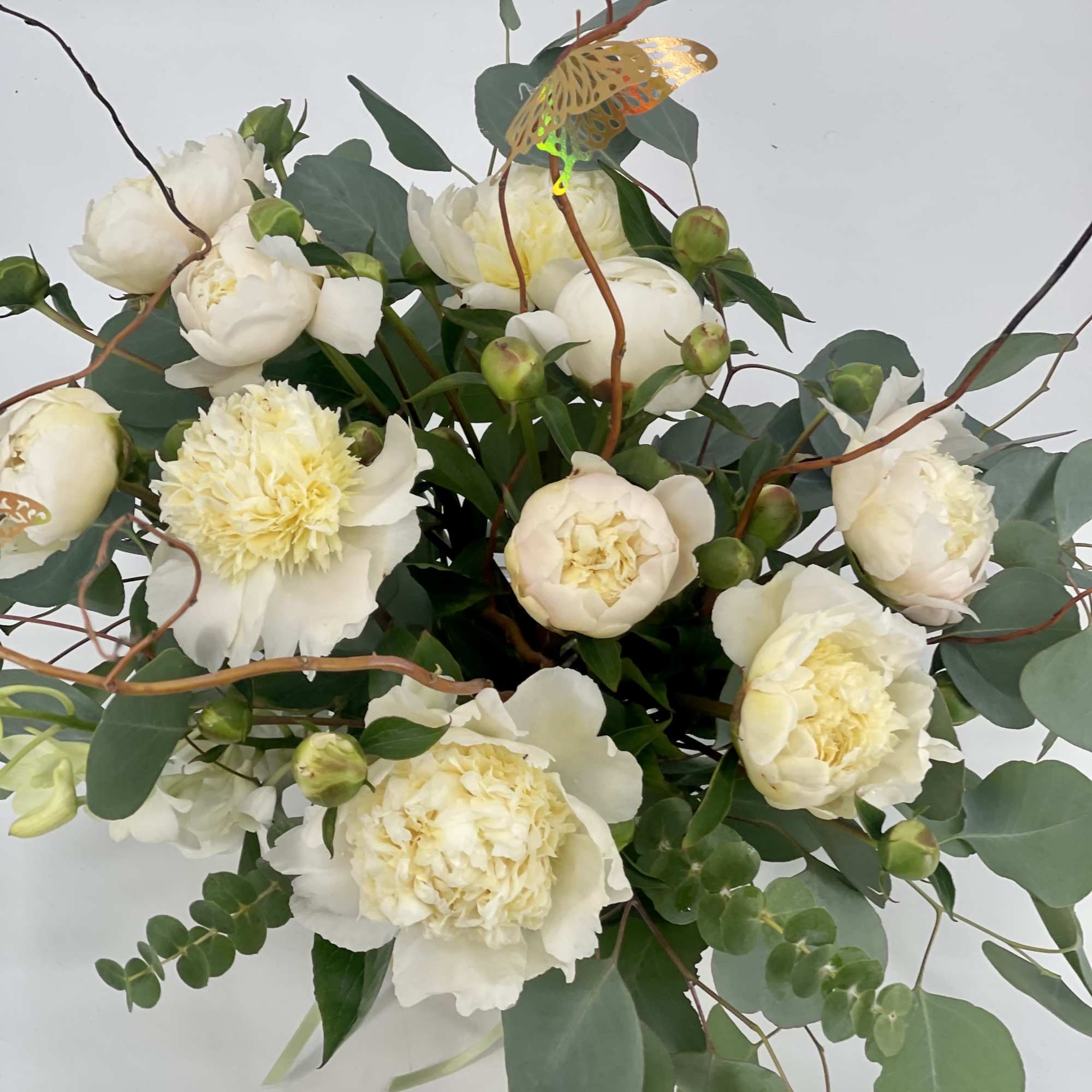 Cream peonies and white blooms arranged with eucalyptus and curly branches