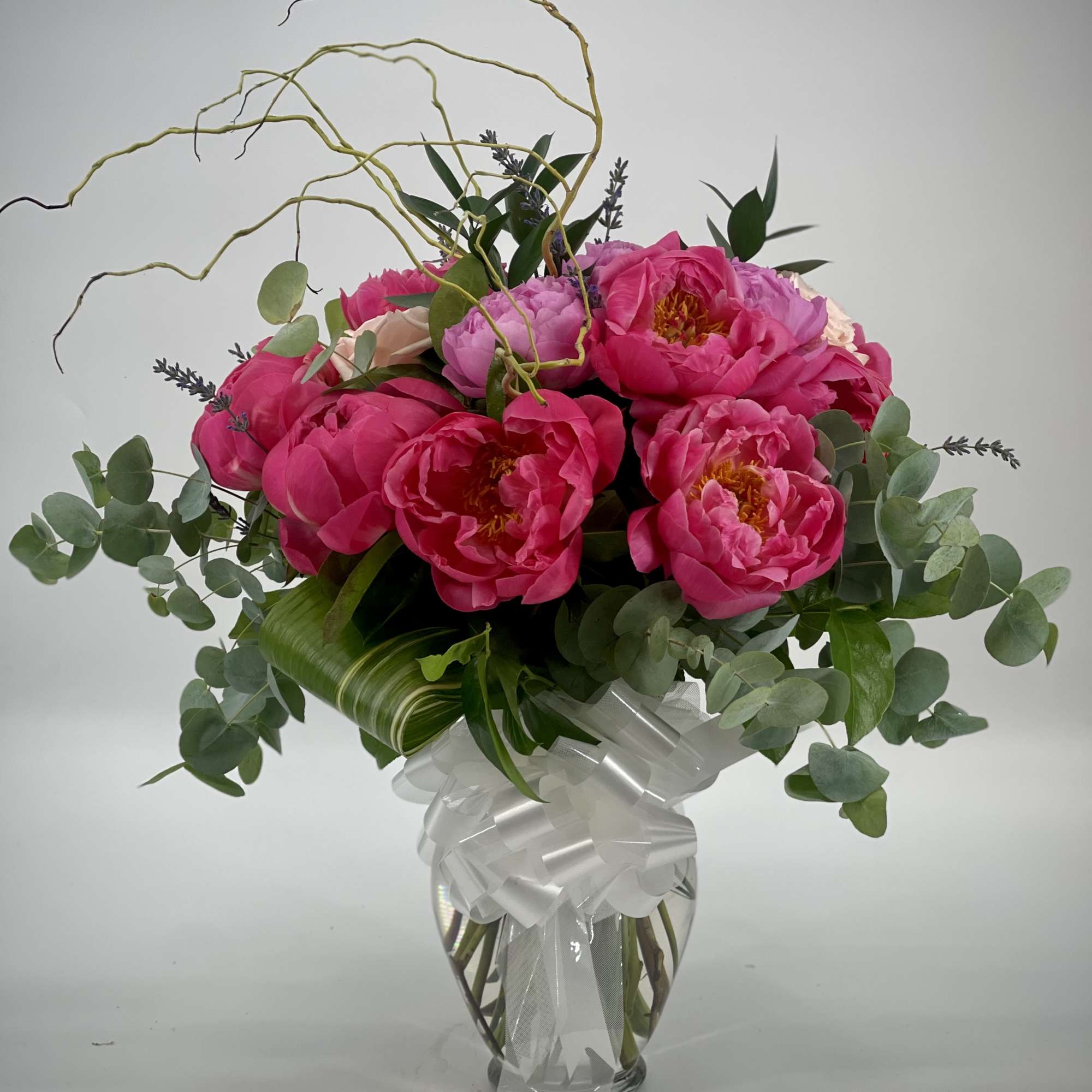 Pink peony bouquet in a clear glass vase with a white ribbon