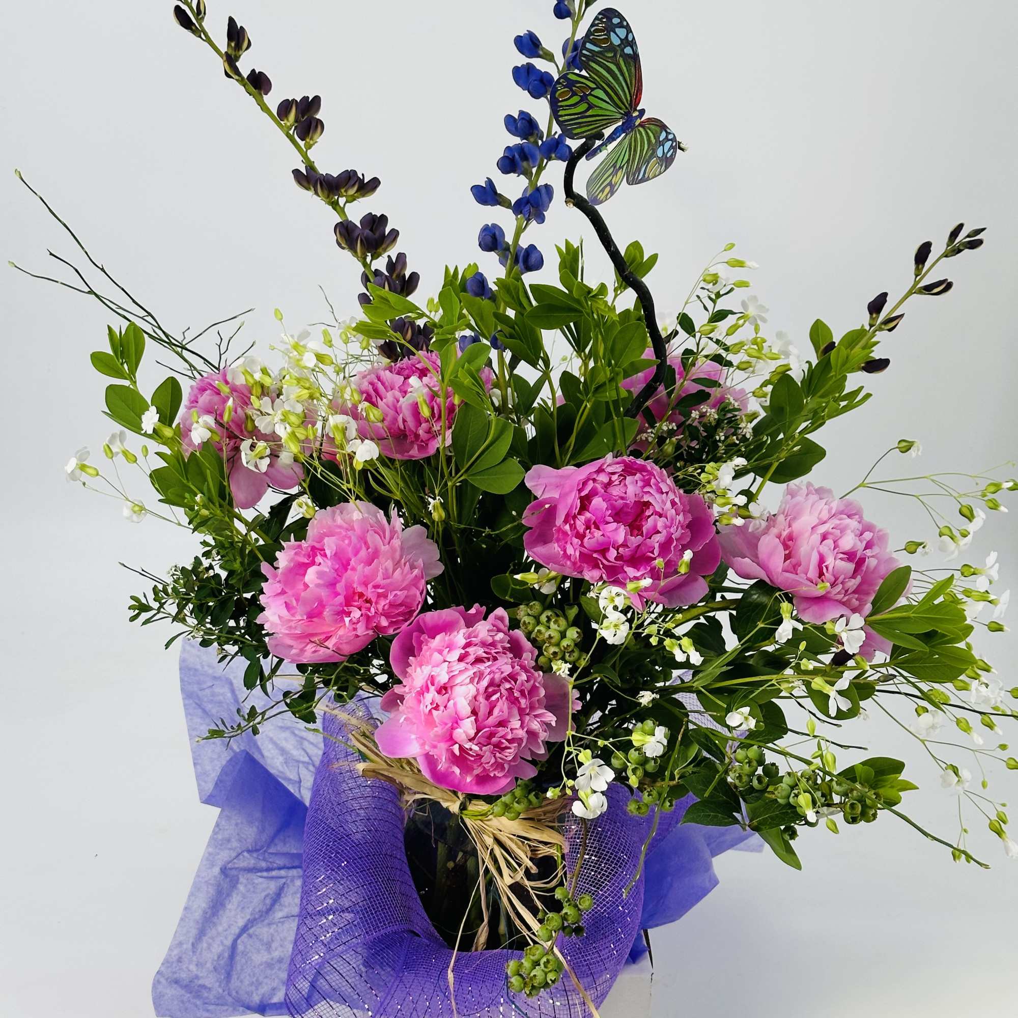 Pink peonies in a purple-wrapped bouquet with a butterfly pick