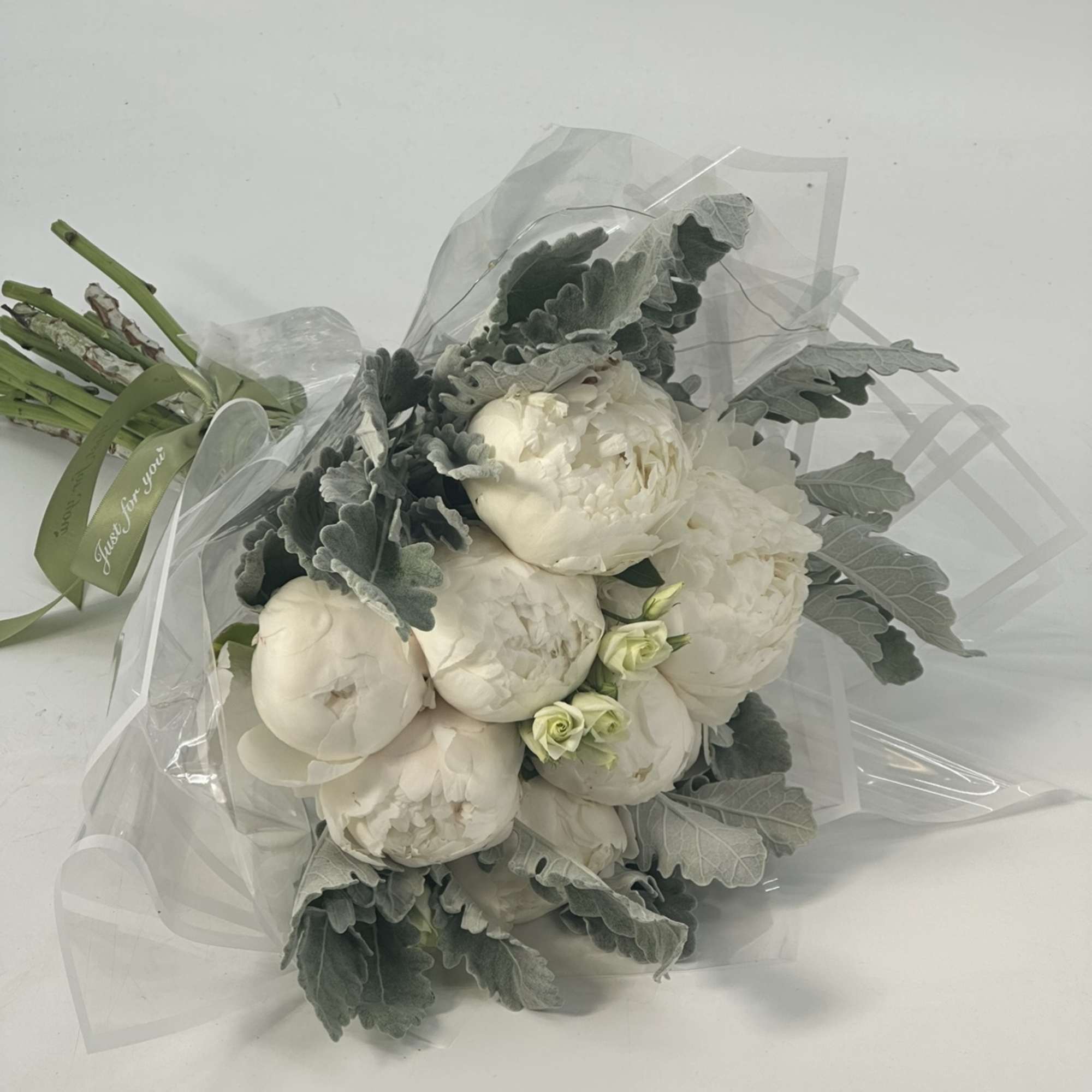 Bouquet of white peonies with silvery foliage wrapped in clear plastic