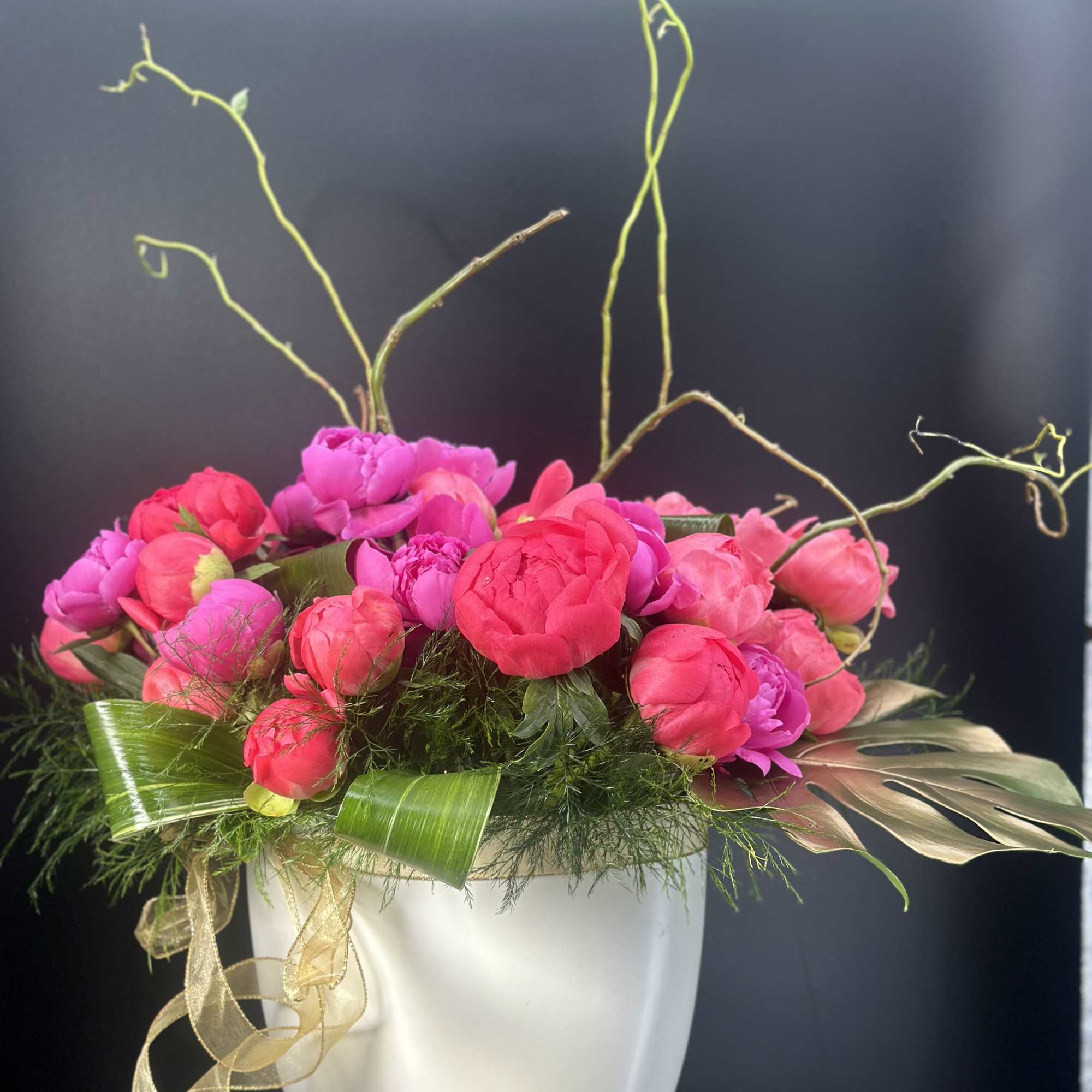 Pink peonies arranged in a white vase with gold ribbon