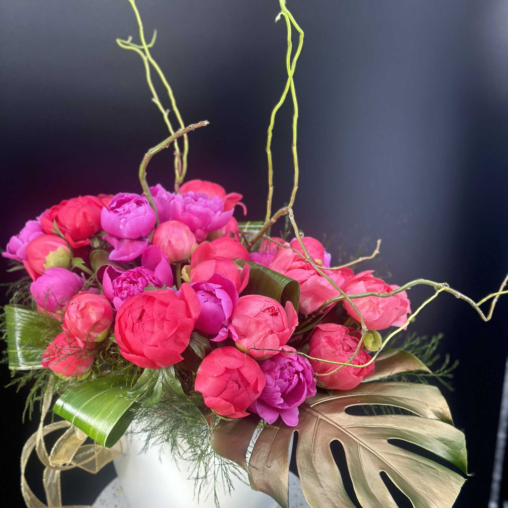 Pink peonies arranged in a white vase with large tropical leaves