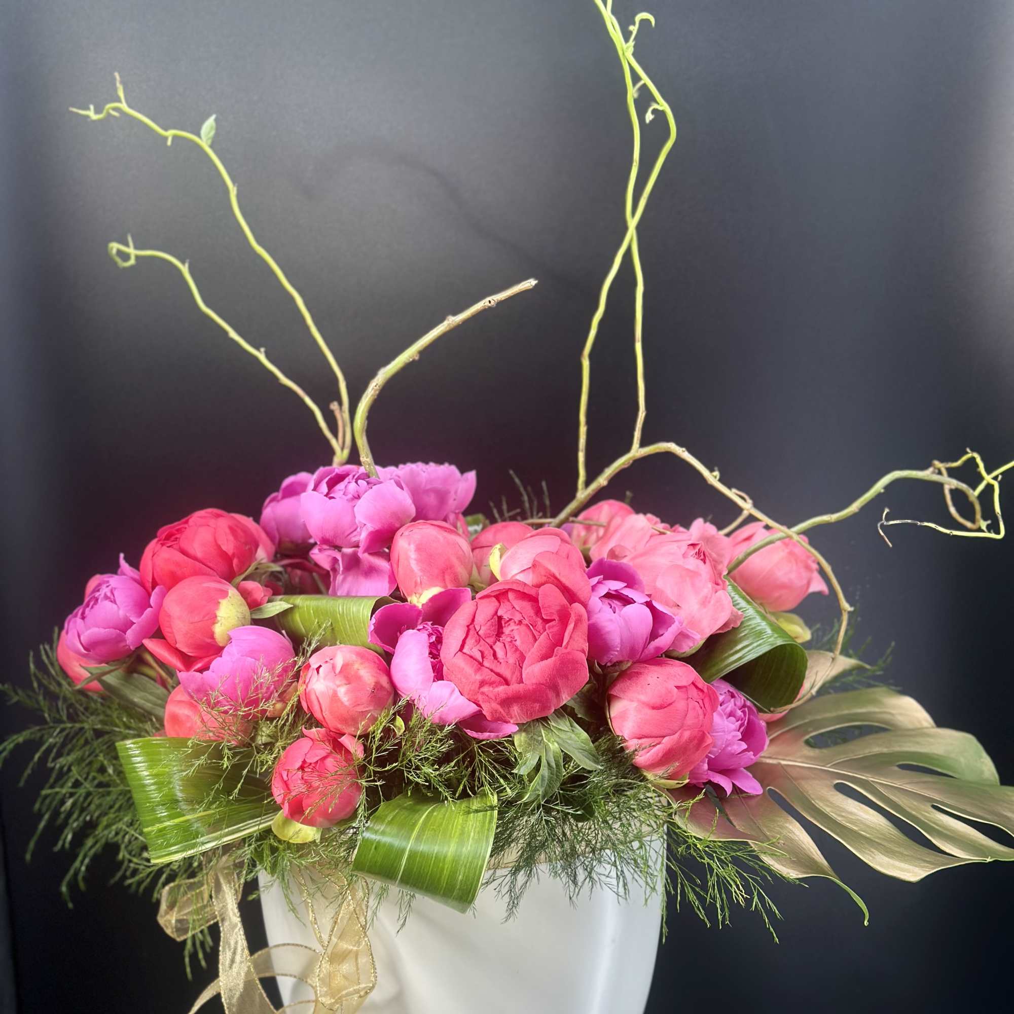 Pink and magenta peonies arranged in a white vase with curly branches