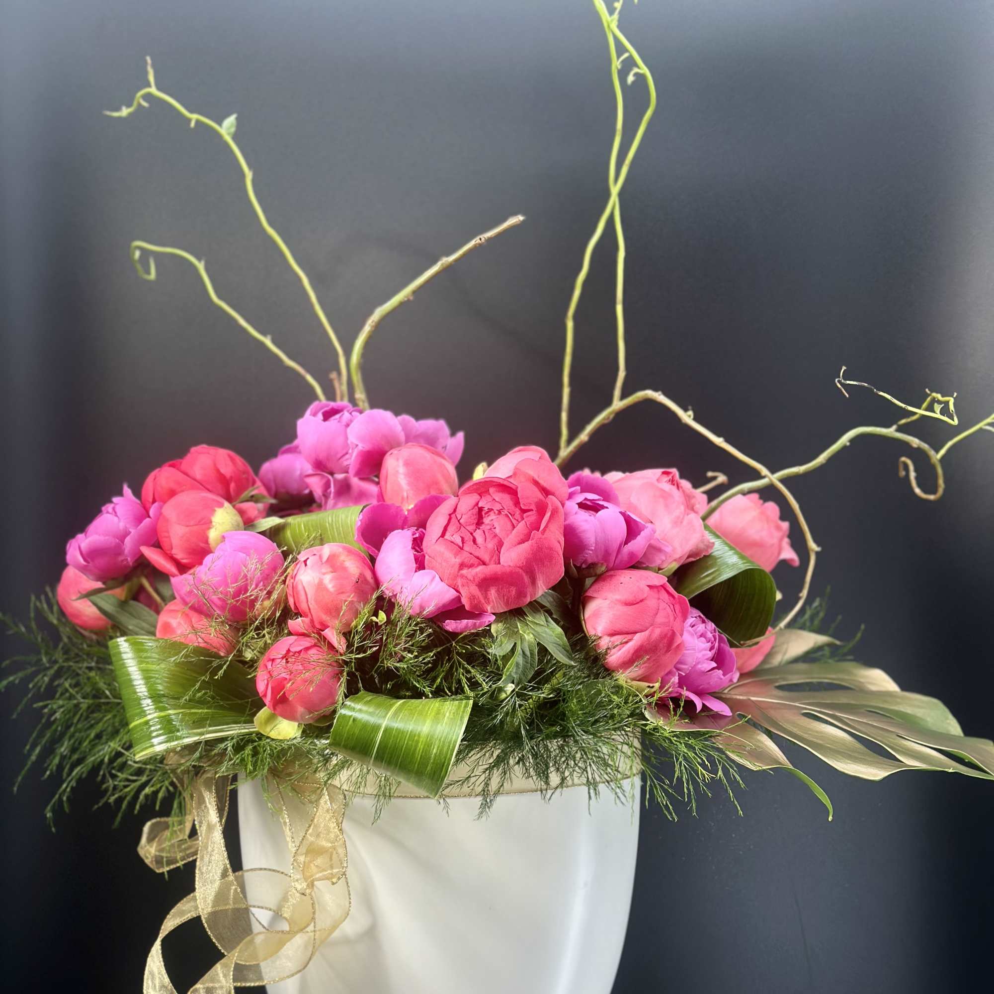 Pink and magenta peonies arranged in a white vase with curly branches