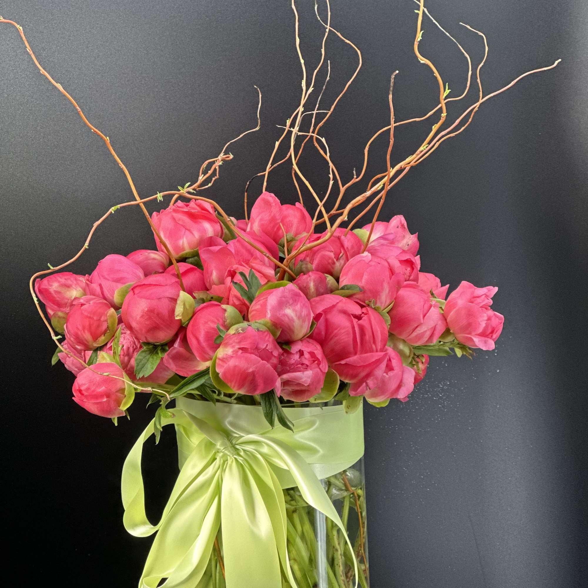 Pink peonies in a clear glass vase with a pale green ribbon