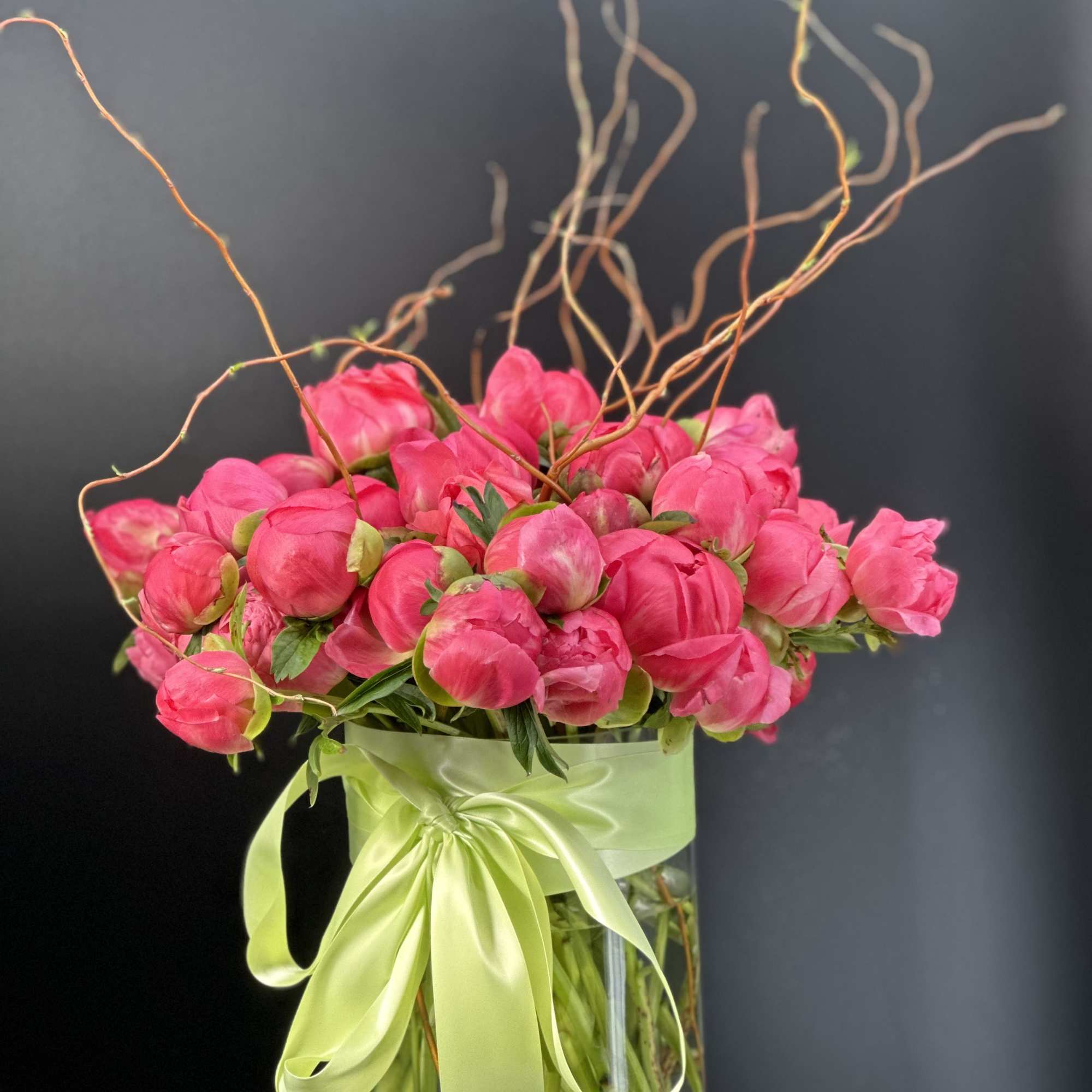 Pink peonies arranged in a clear glass vase with a pale green ribbon.