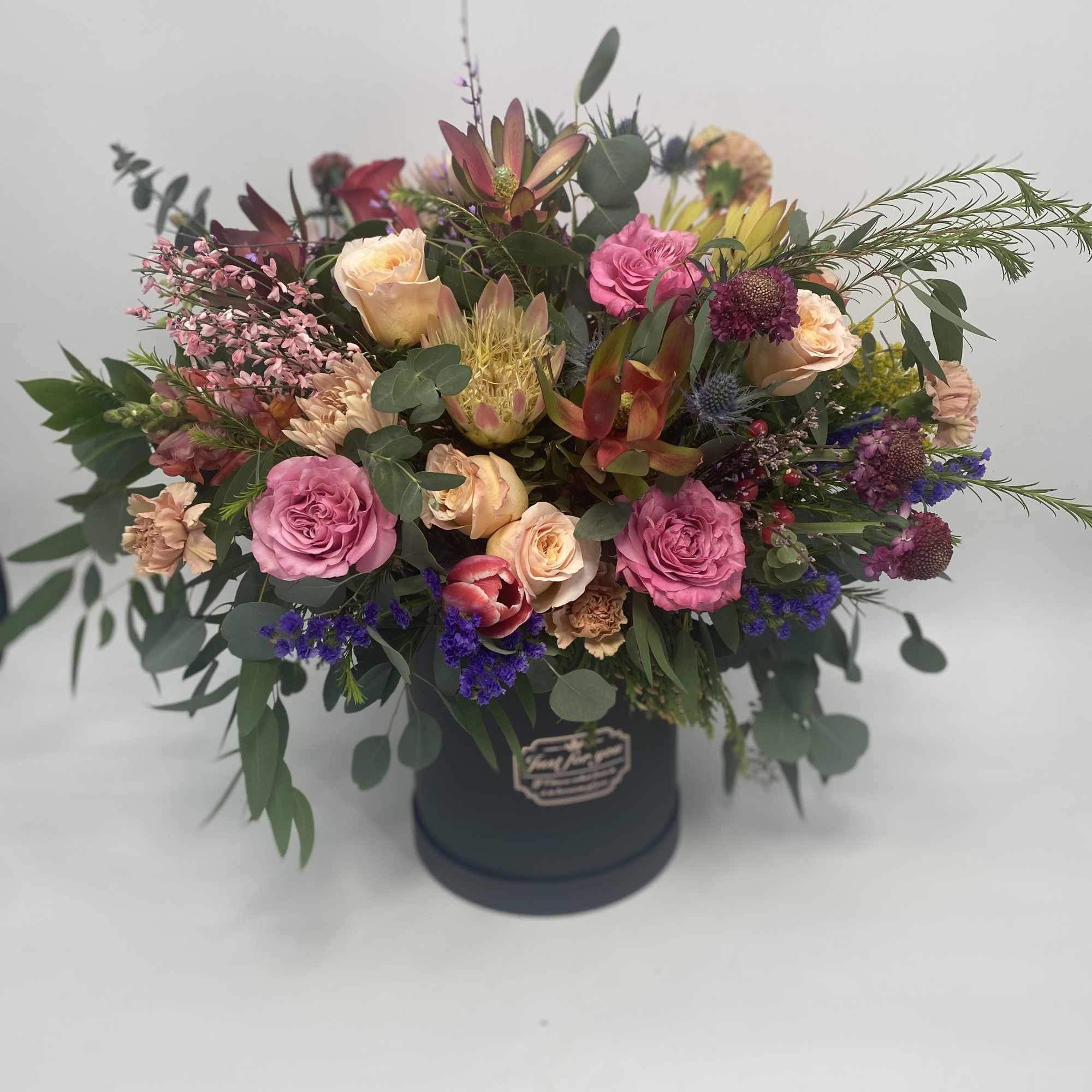 Mixed bouquet in a dark round box with pink and peach blooms