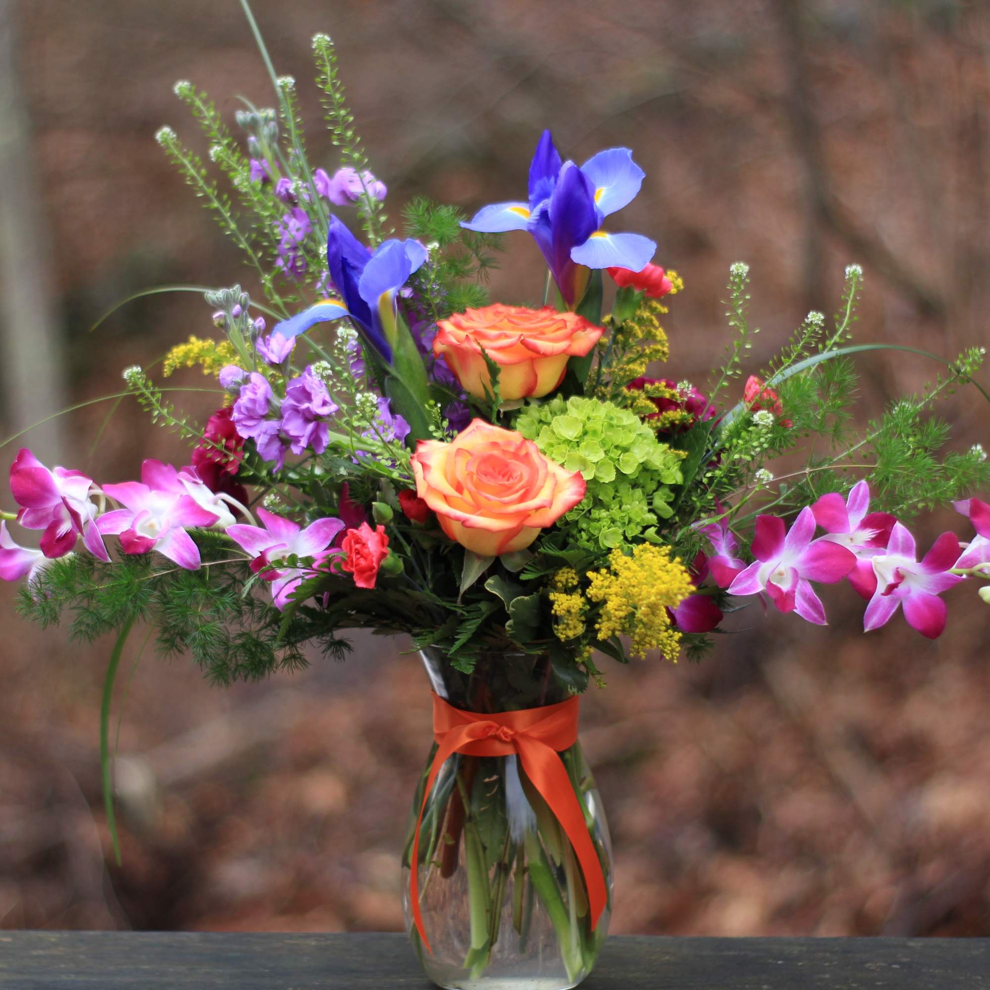Colorful bouquet in a glass vase with orange roses and purple orchids