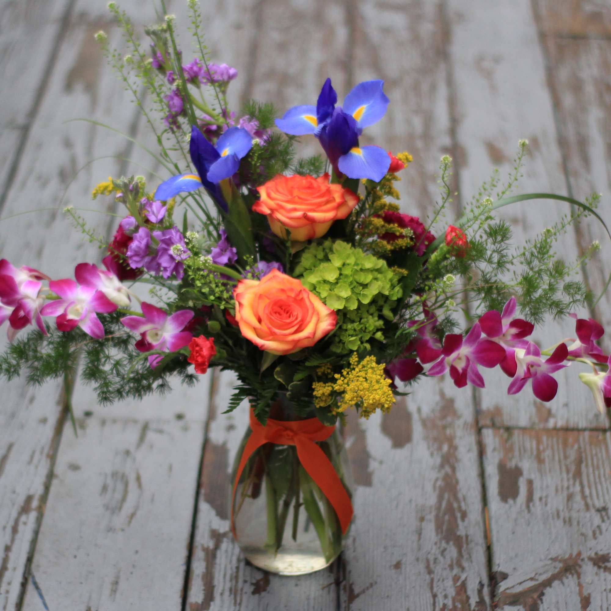 Colorful bouquet with orange roses and purple orchids in a glass vase