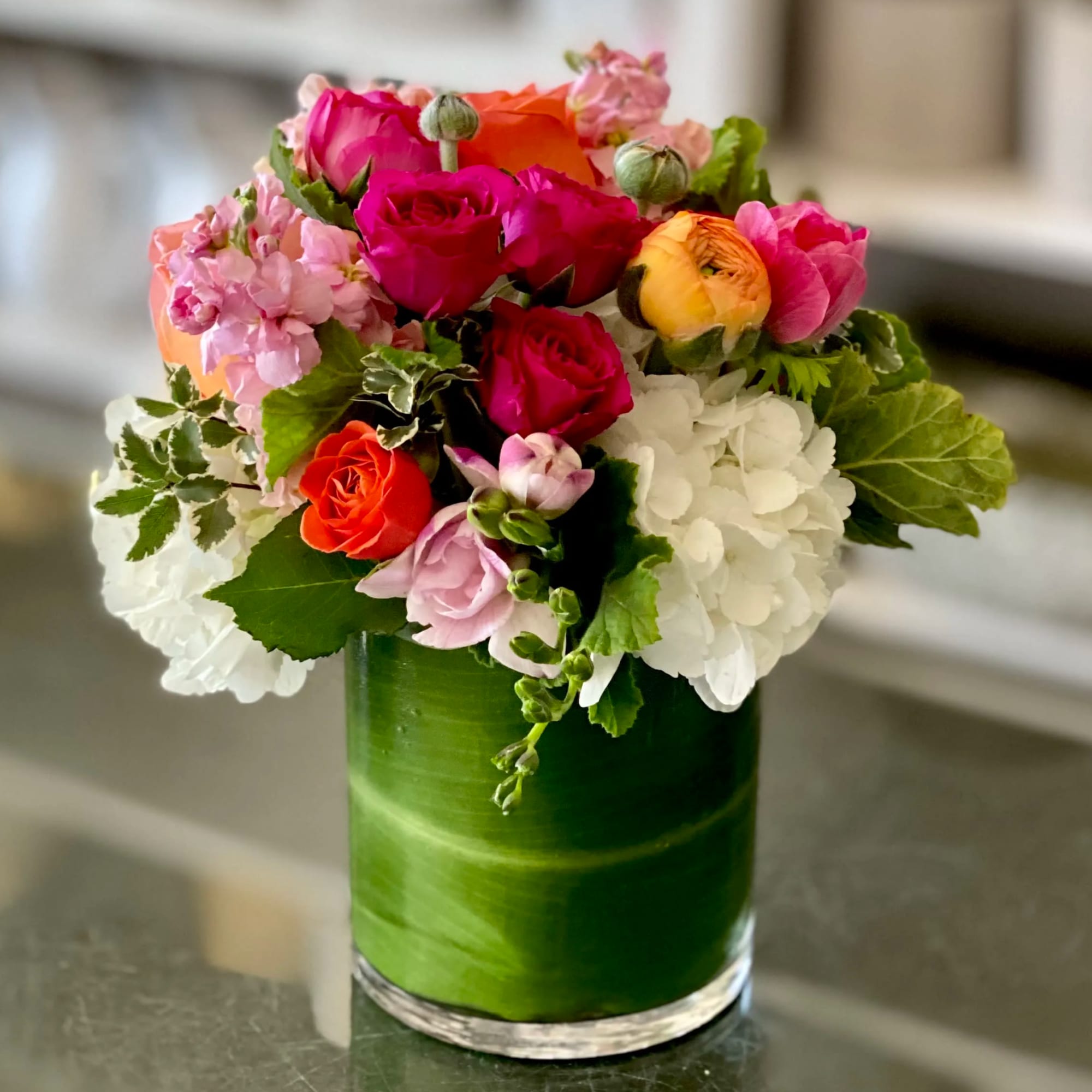 Mixed bouquet of roses, hydrangeas, and ranunculus in a green glass vase