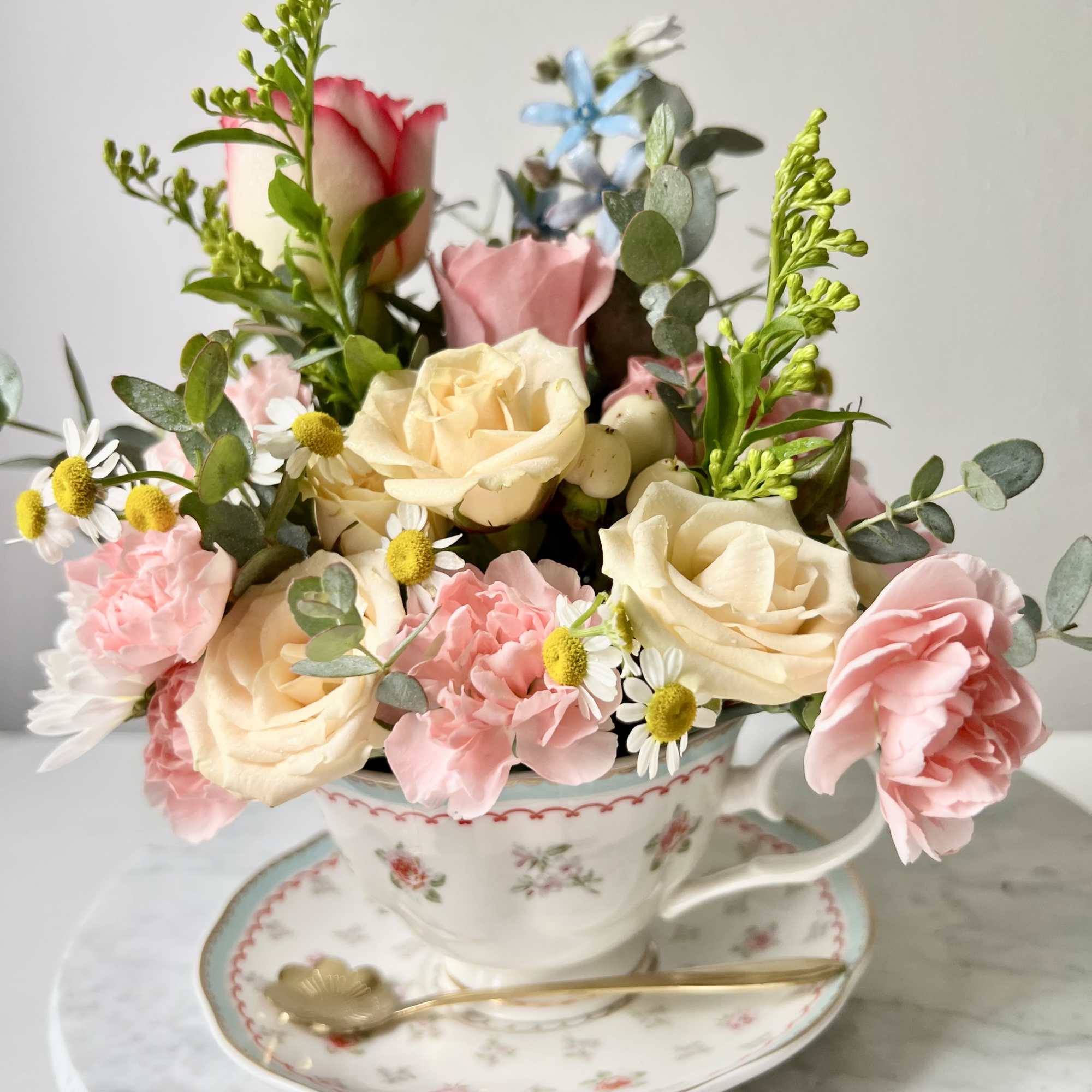 A tea cup filled with roses, carnations, and tiny white daisy-like blooms-this