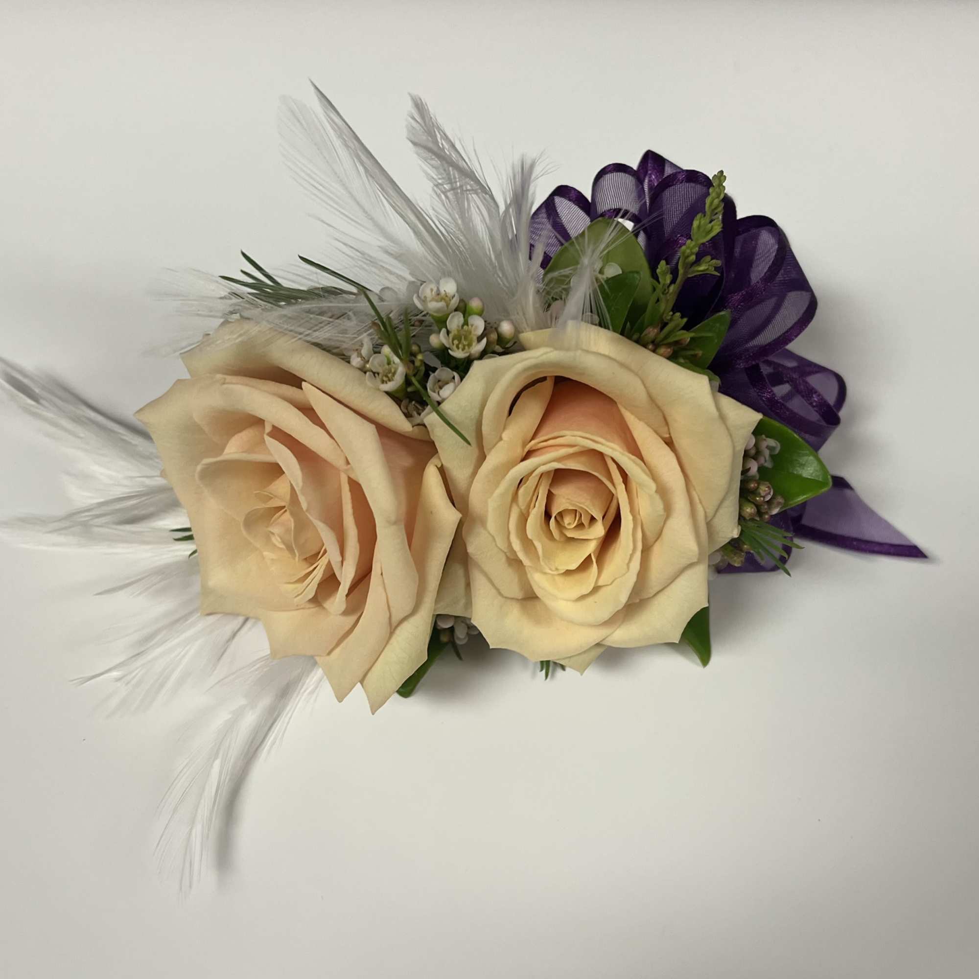 Two cream roses with purple ribbon and white feathers