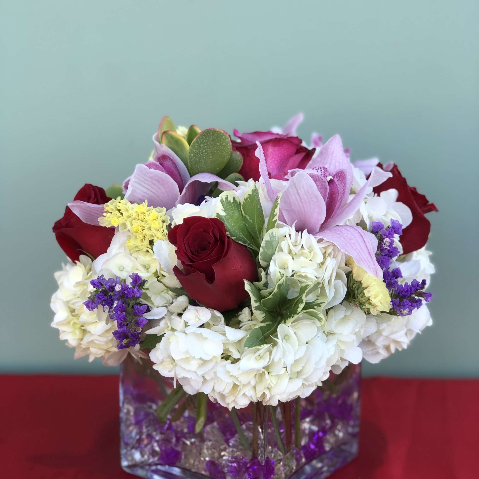 Mixed bouquet of red roses, pink orchids, and white hydrangeas in a glass vase