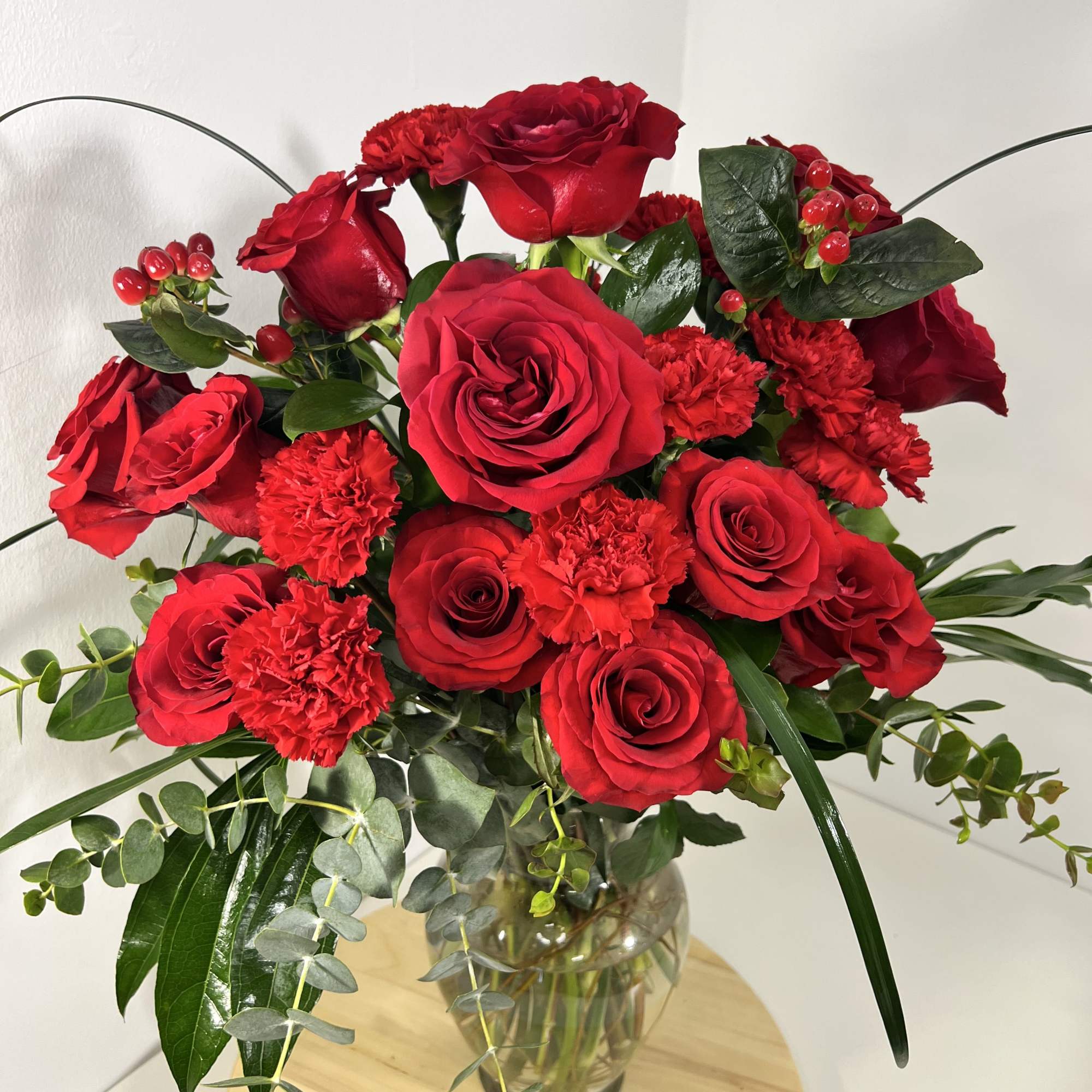 Vivid red roses and matching red carnations form a lush, rounded flower