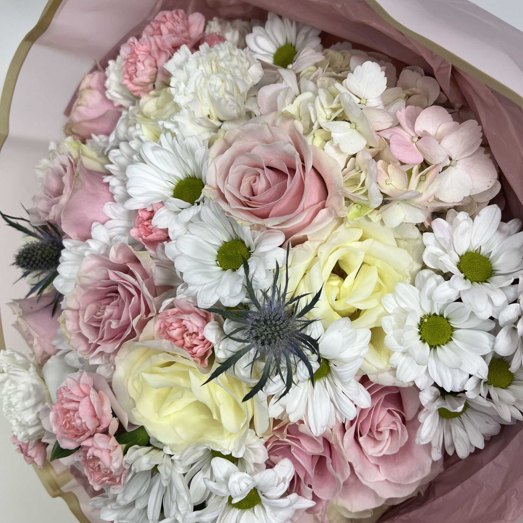 Soft blush roses and airy white daisy blooms make this hand-tied flower