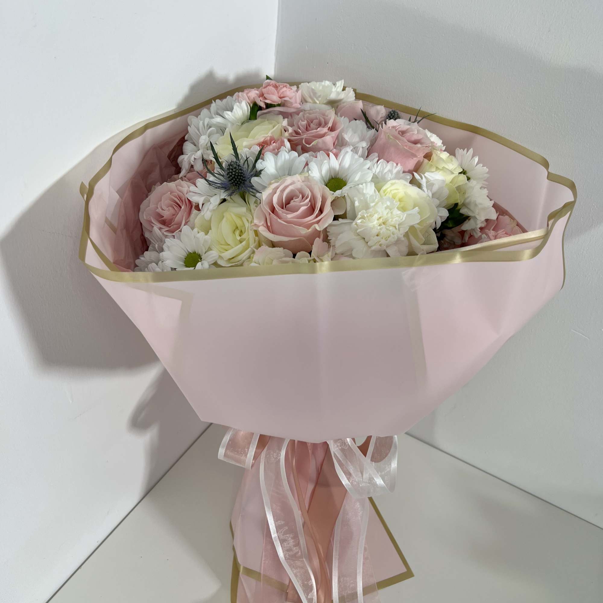 Soft blush roses and airy white daisy blooms make this hand-tied flower