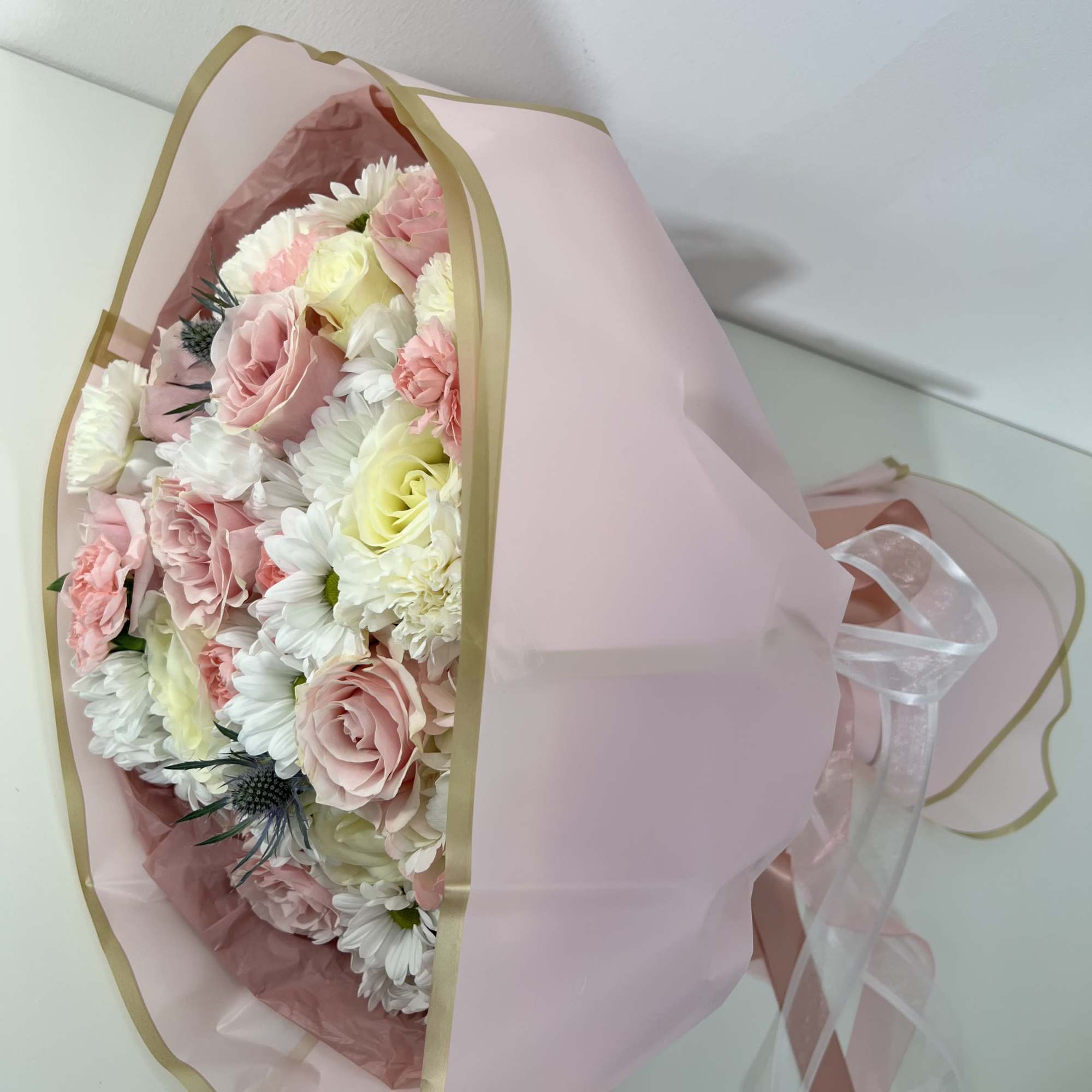 Soft blush roses and airy white daisy blooms make this hand-tied flower