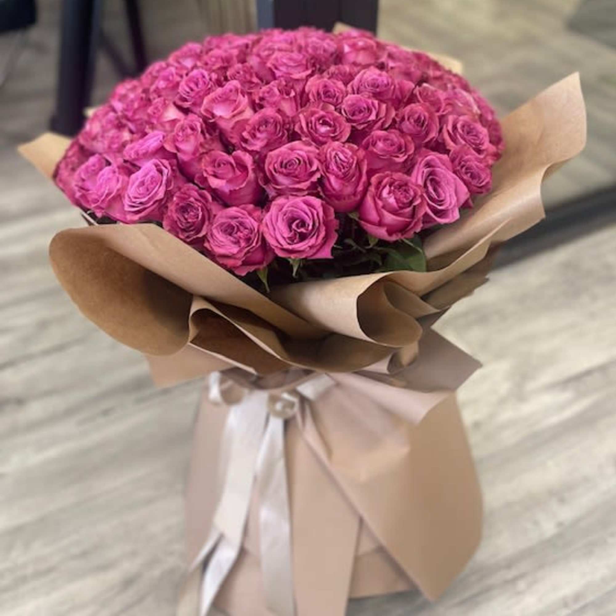Large bouquet of pink roses wrapped in tan paper with a ribbon