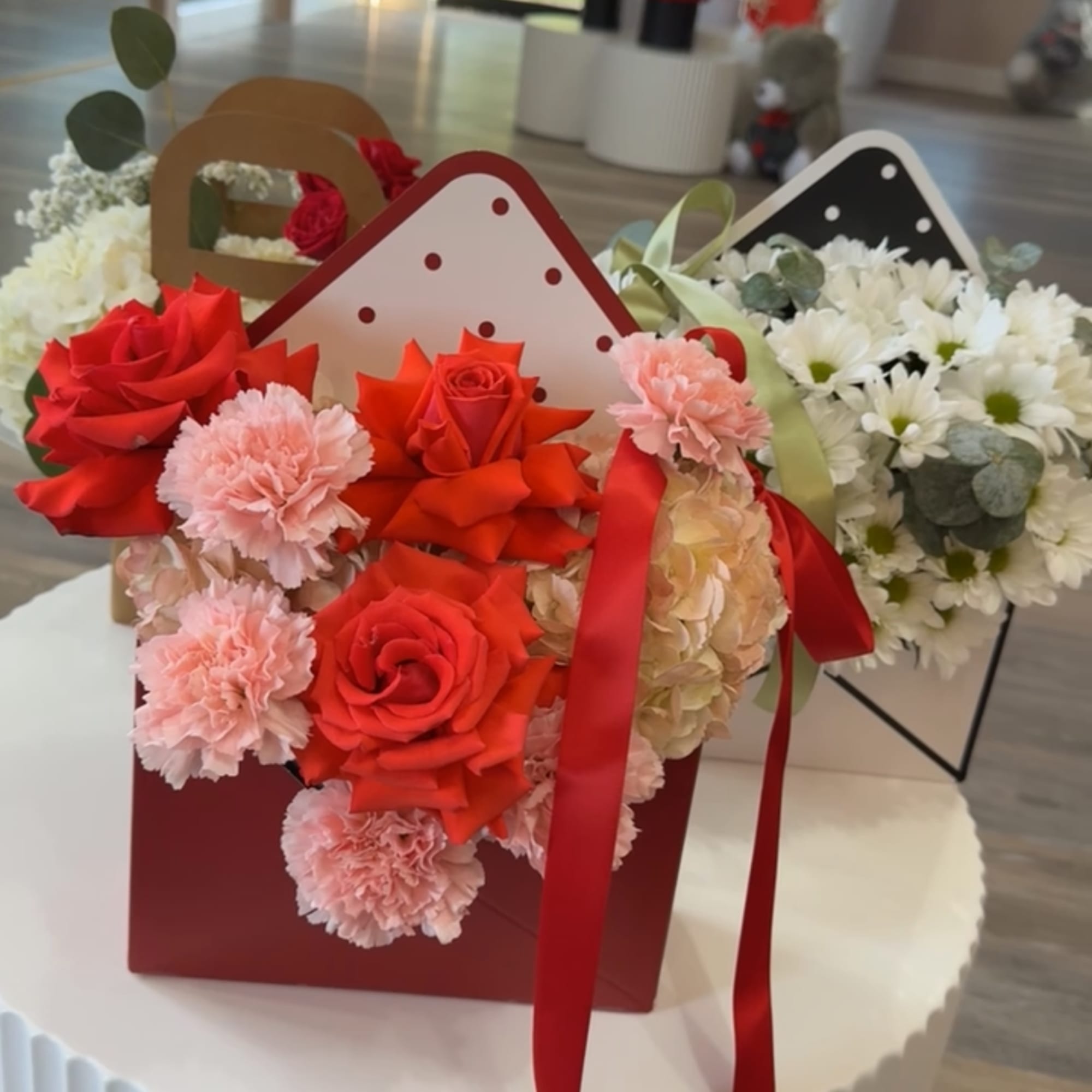 A clustered display of red roses, pink carnations, white daisies and pale
