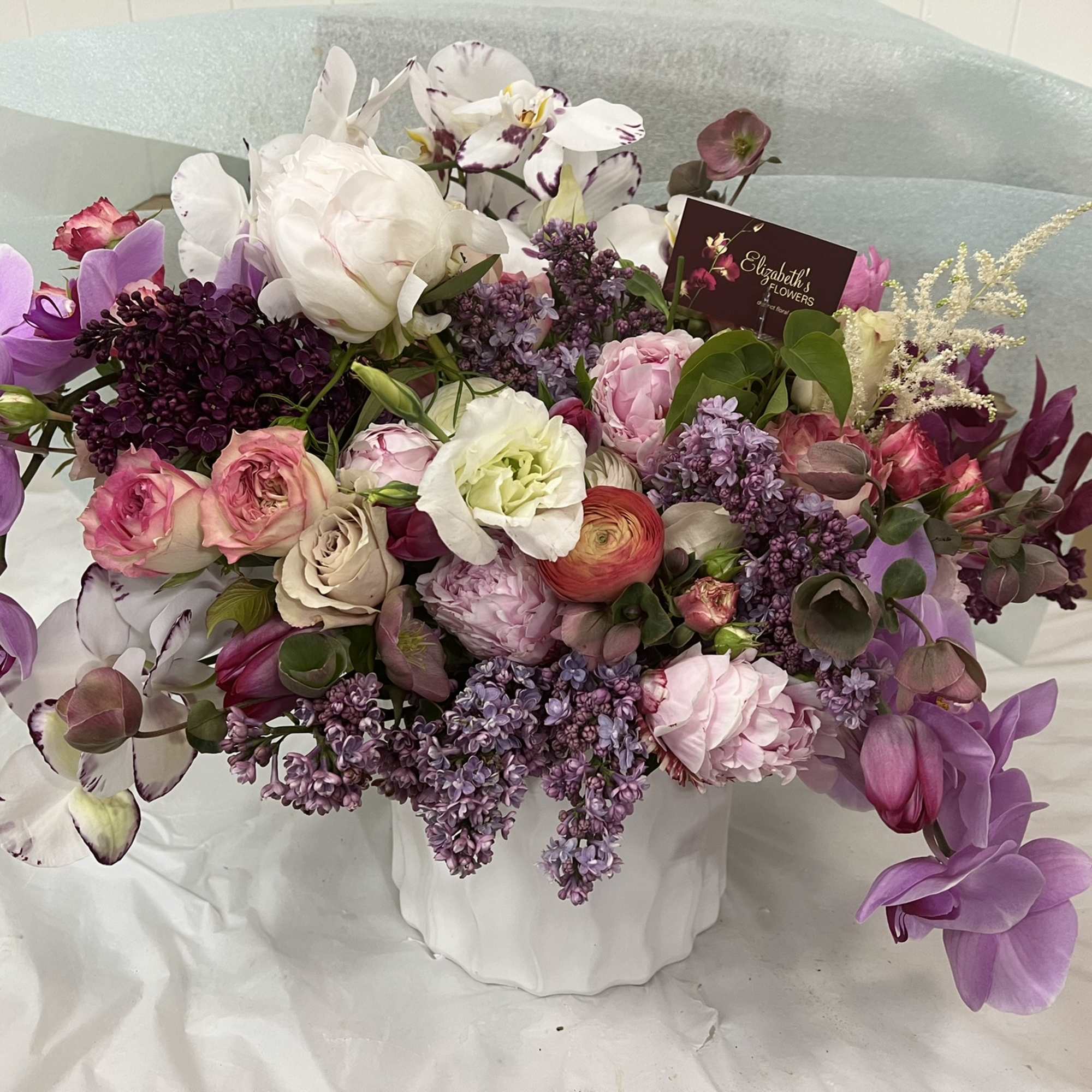 Mixed bouquet of pink, purple, and white flowers in a white vase