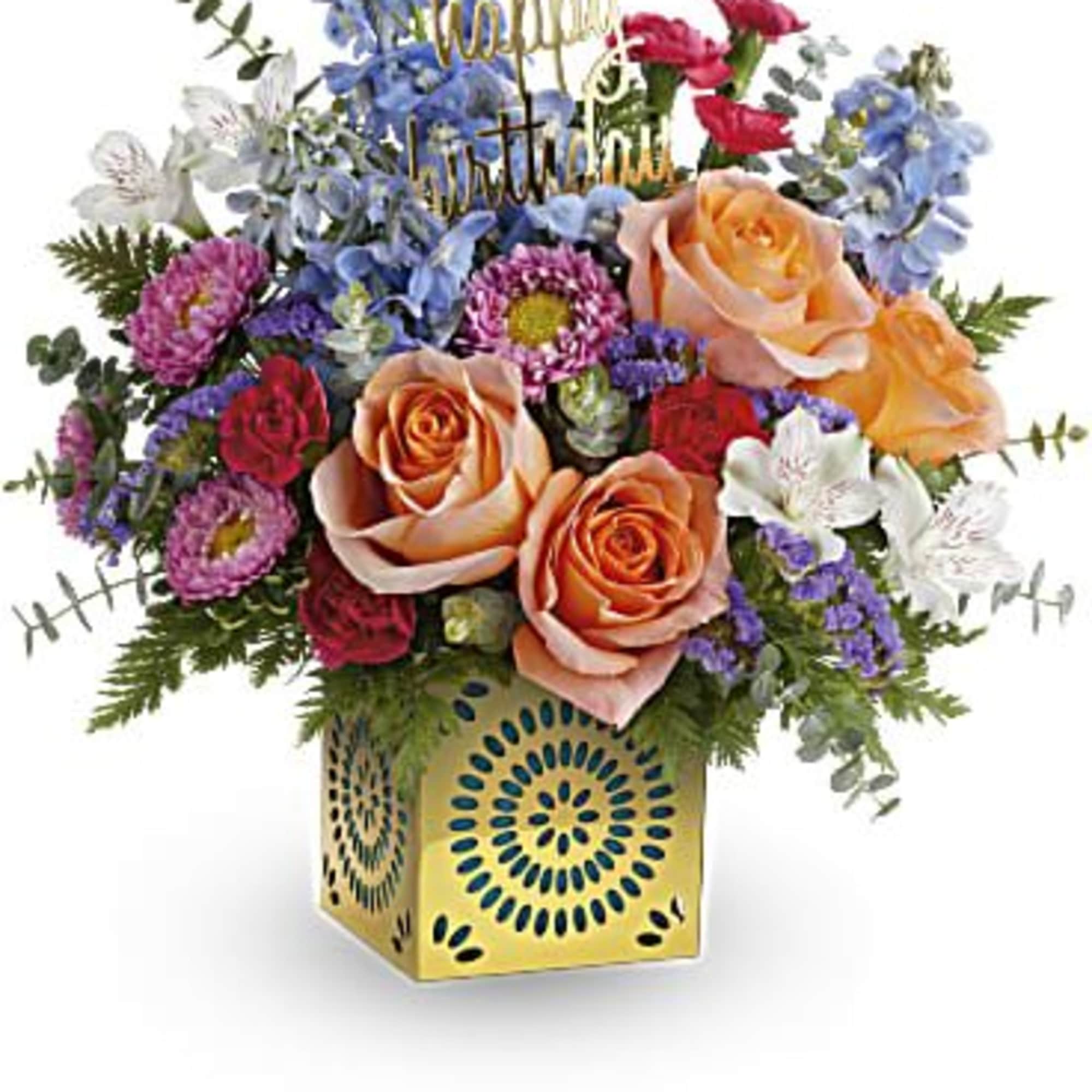 Colorful birthday flower arrangement with peach roses and mixed blooms in a yellow patterned cube vase