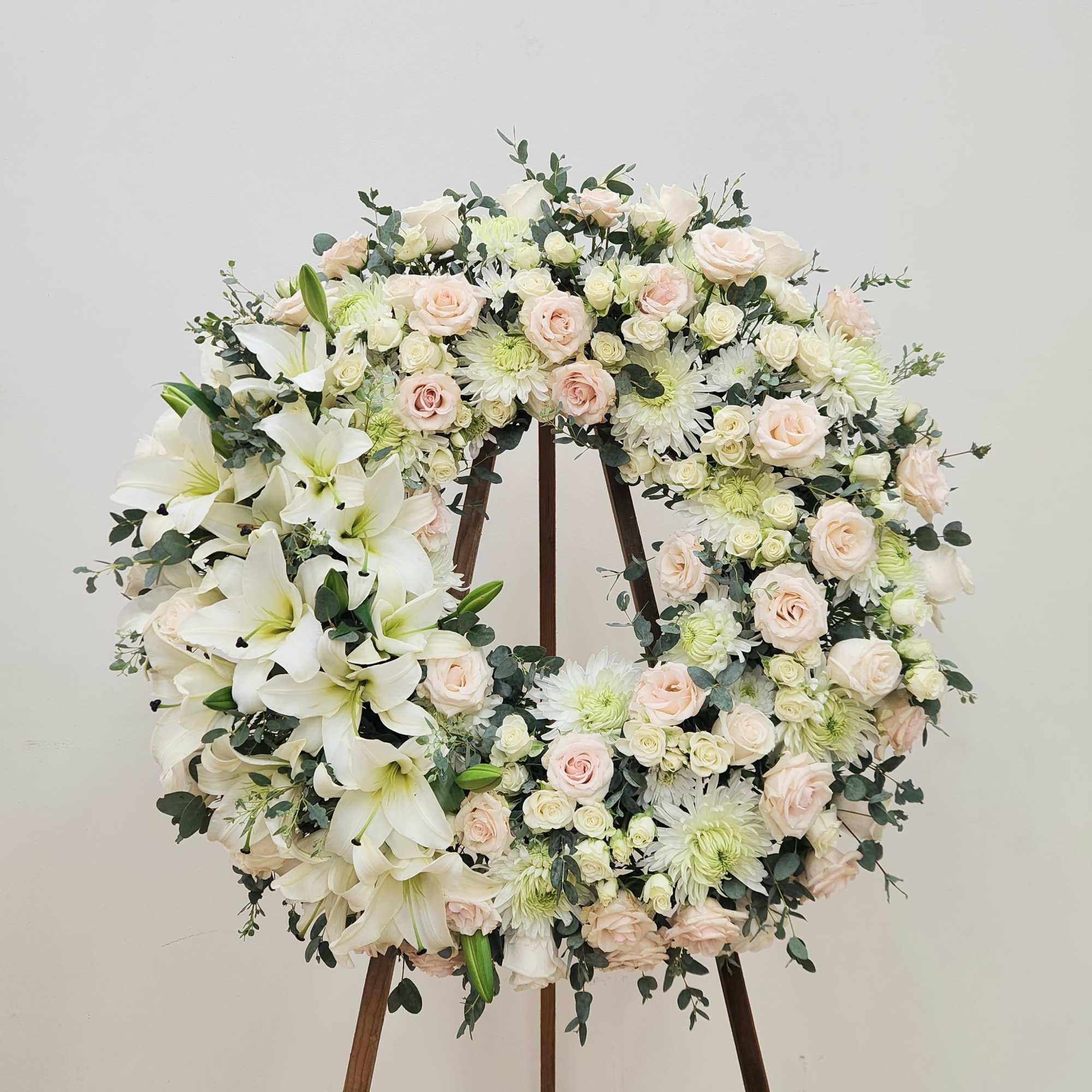 A large circular wreath of white lilies, blush roses, spray roses and