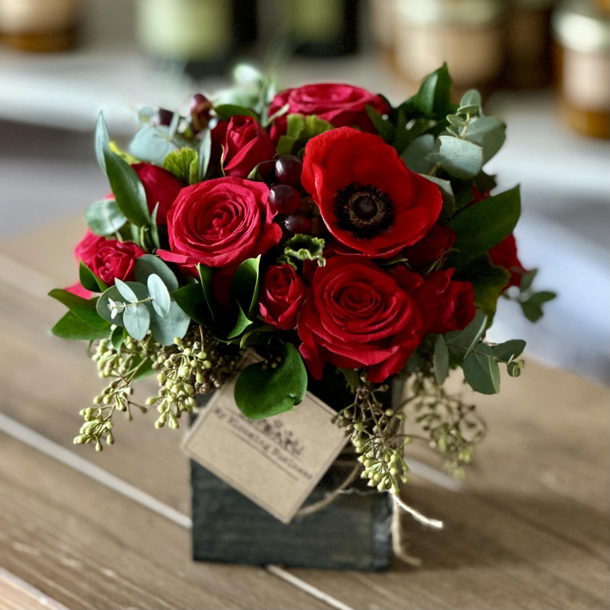 Red rose bouquet with a red anemone in a small square vase