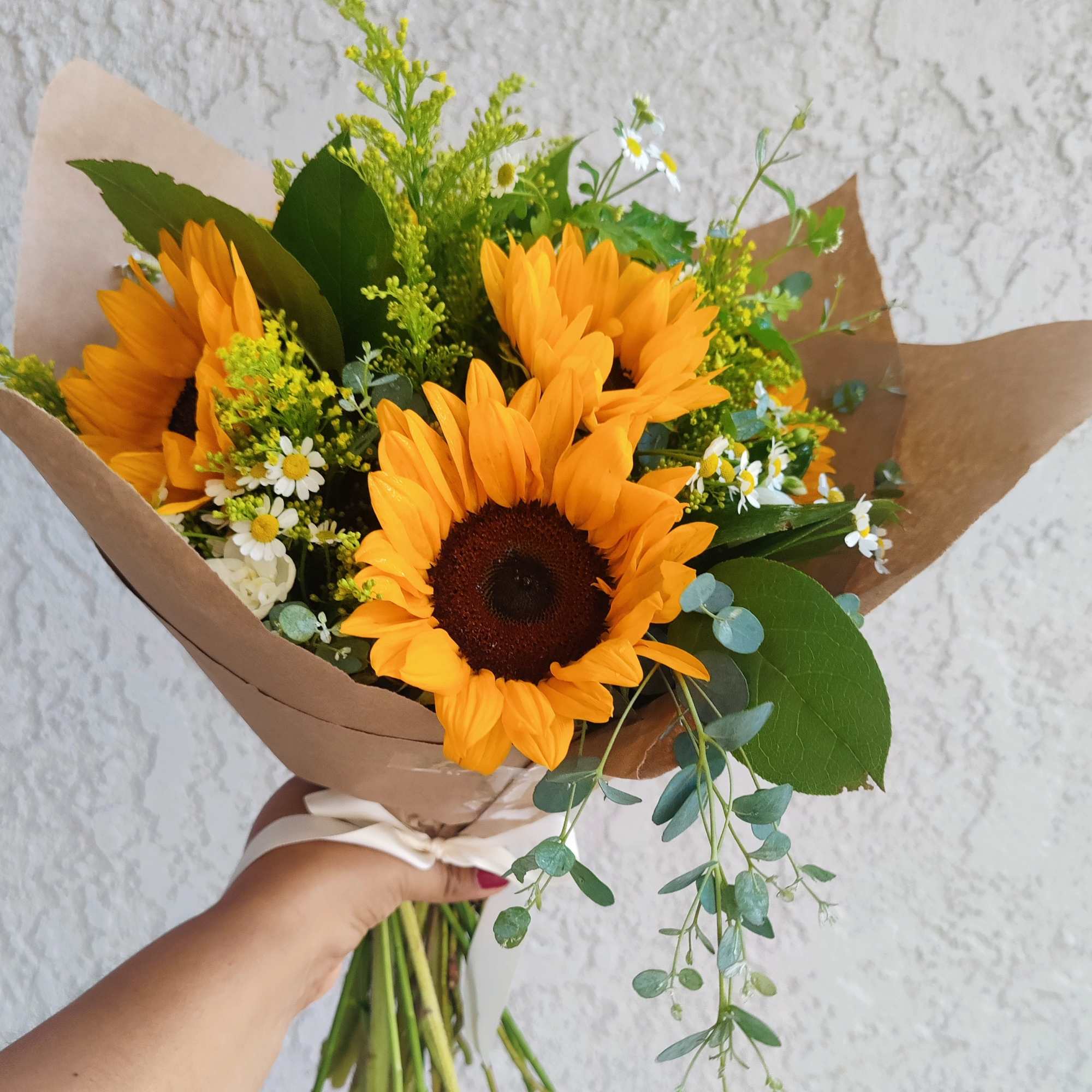 Handheld bouquet of sunflowers with small white daisies and brown paper wrap