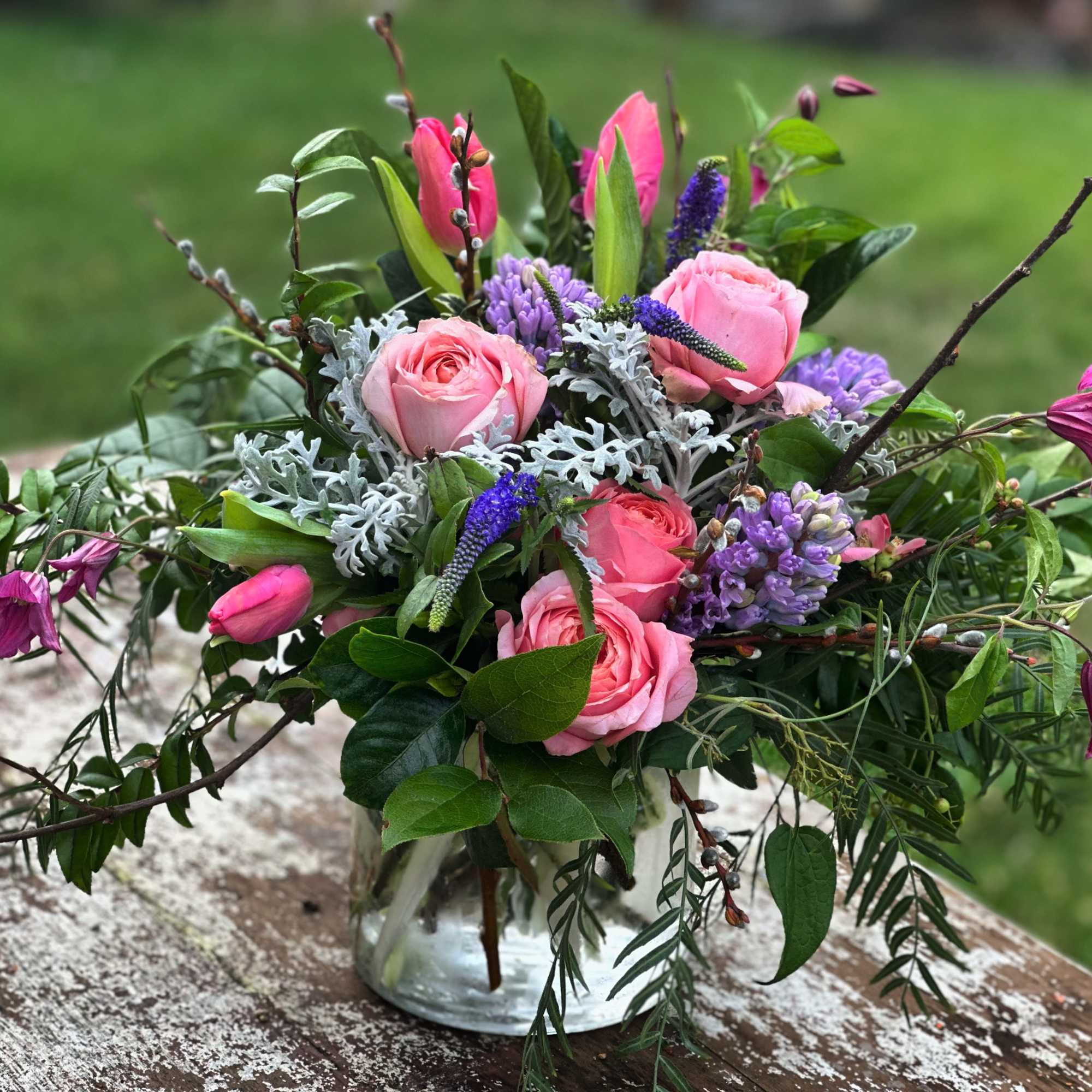 Pink roses and purple flowers in a clear glass vase with branches