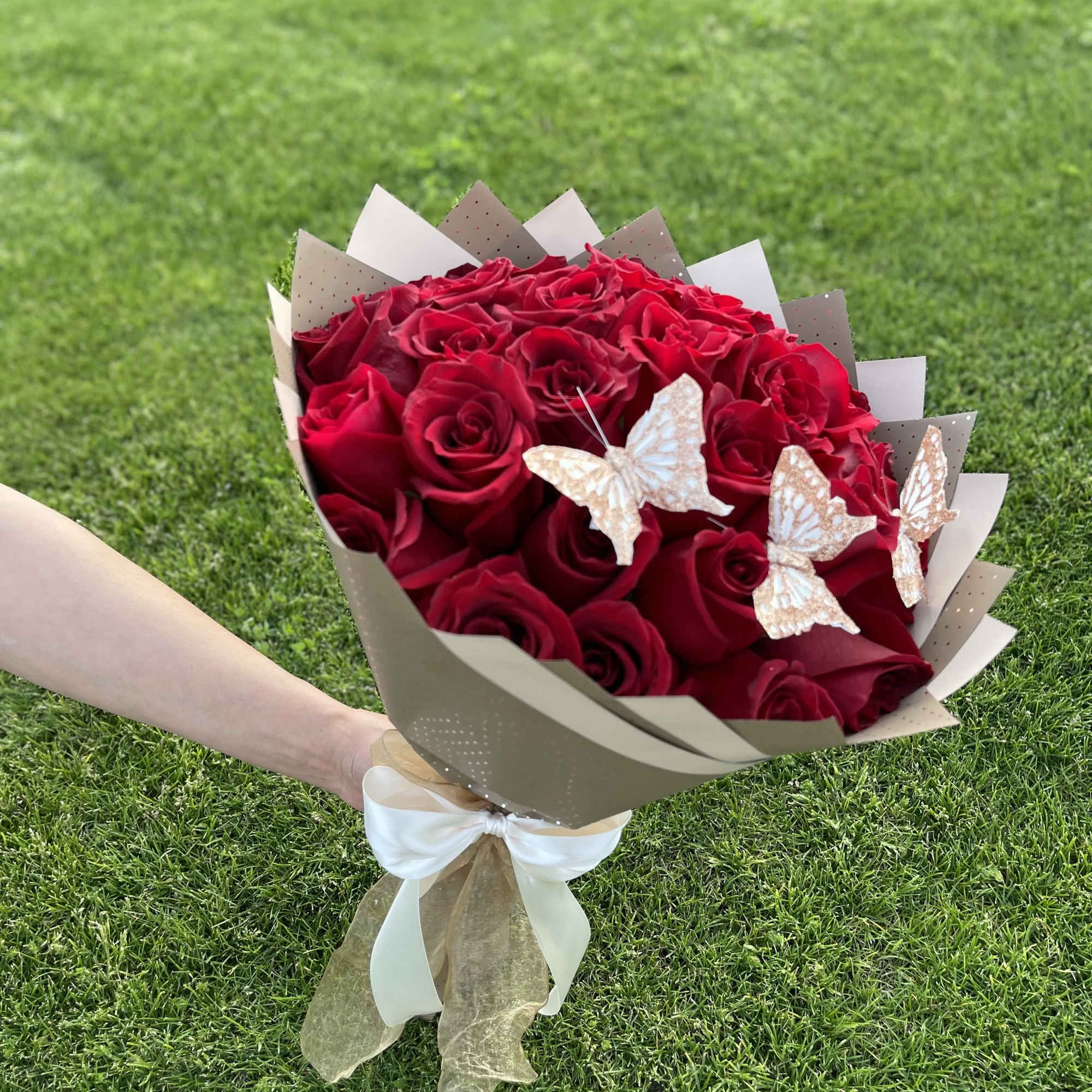 Bouquet of red roses wrapped in beige paper with butterfly accents