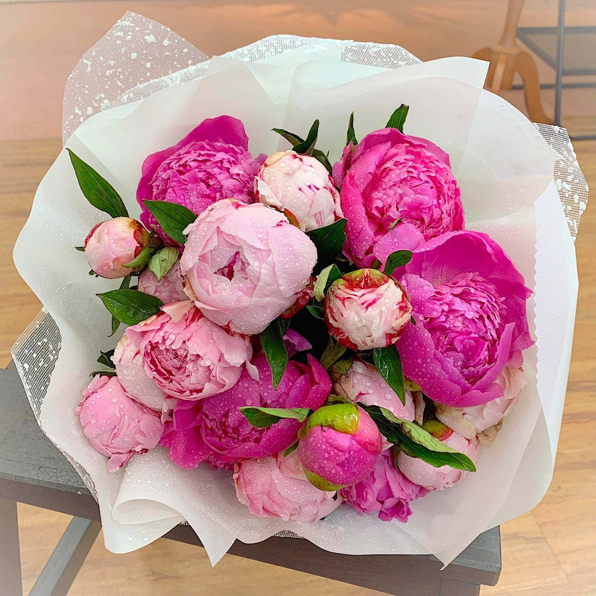 Wrapped bouquet of pink peonies with water droplets in white paper