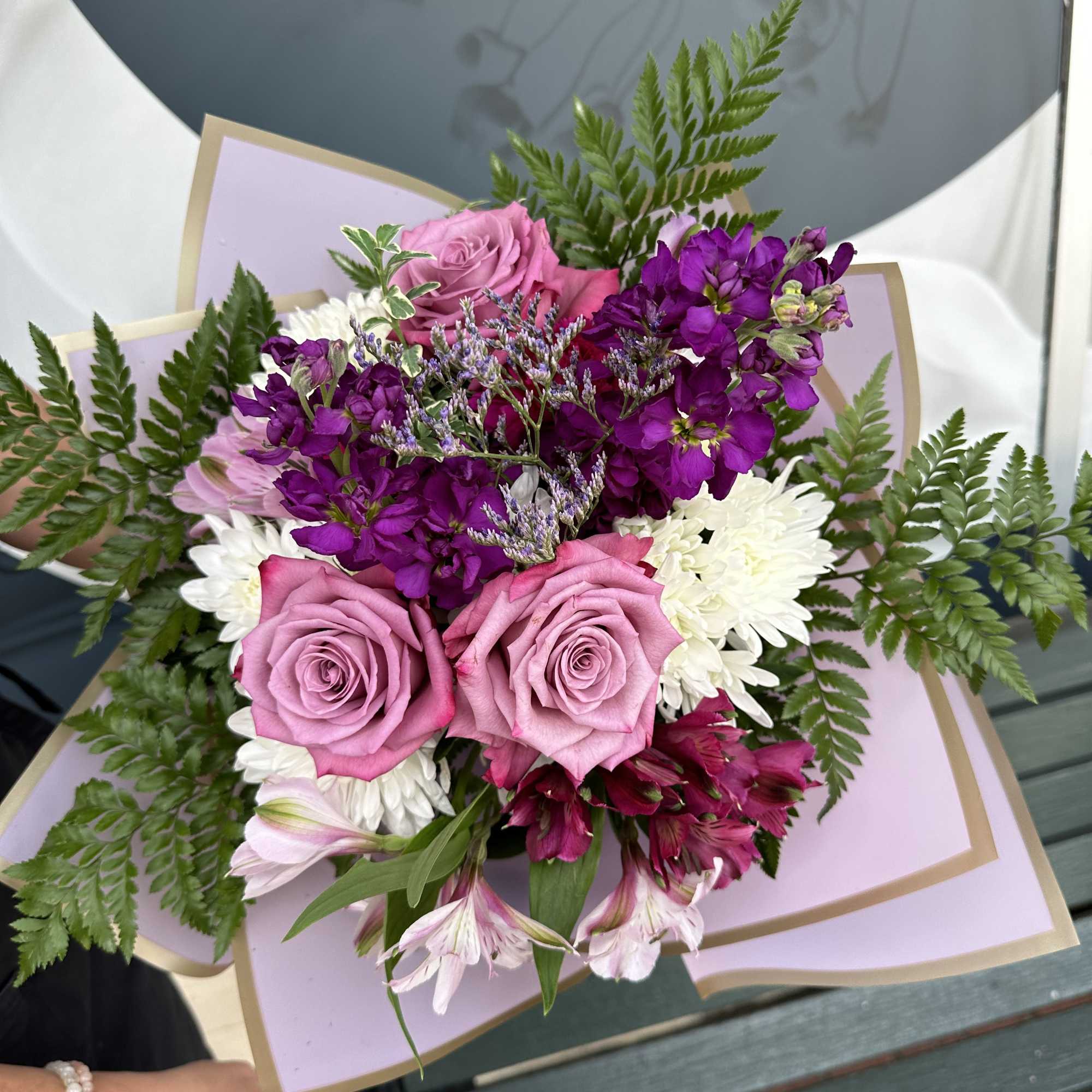 Bouquet of pink roses, purple blooms, and white flowers wrapped in pastel paper