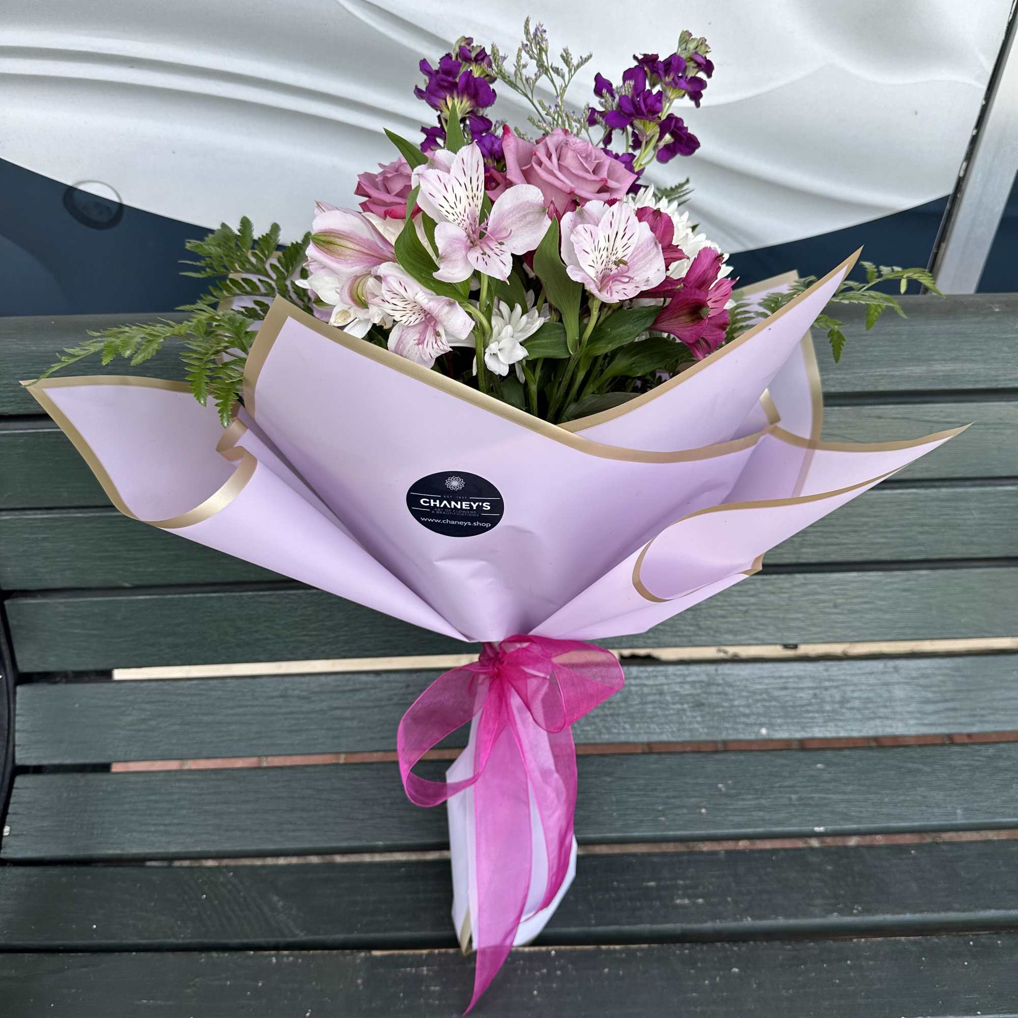 Pink and purple mixed bouquet wrapped in lavender paper with a ribbon