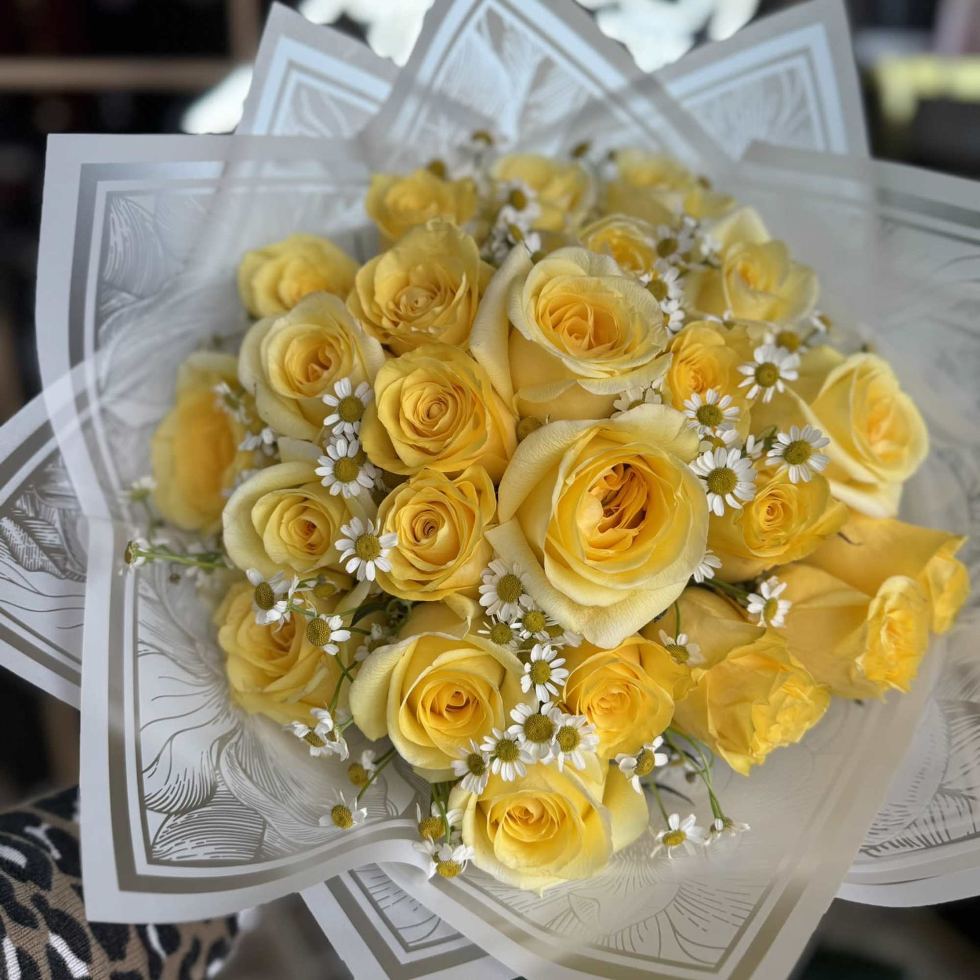 Bouquet of yellow roses with small white daisies wrapped in patterned paper