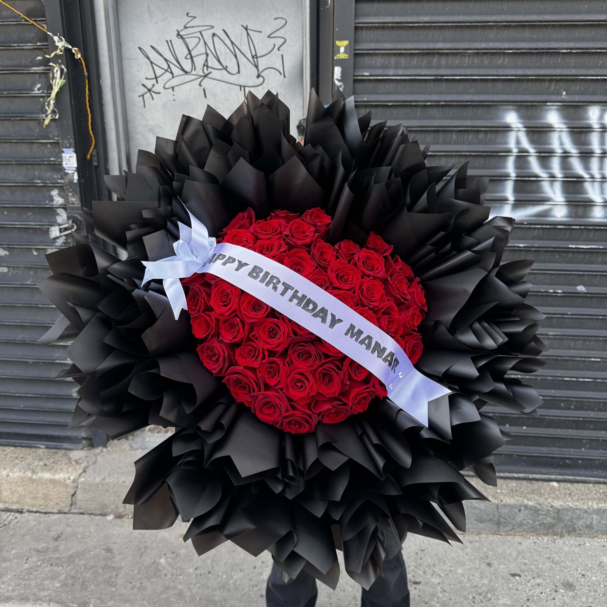 Dense, rounded clusters of velvety red roses wrapped in dramatic black paper