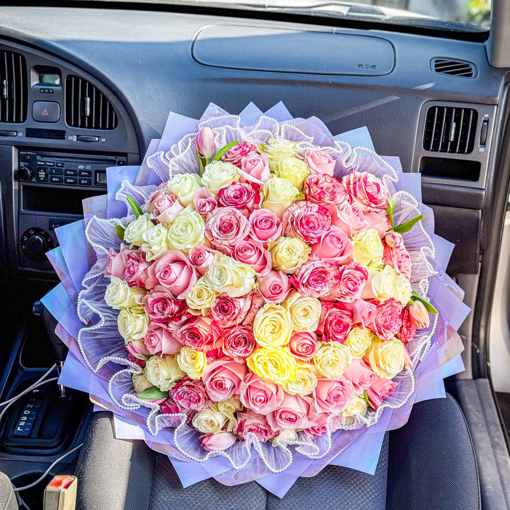 A lush, tightly packed hand-tied bouquet of roses in soft pinks, pale