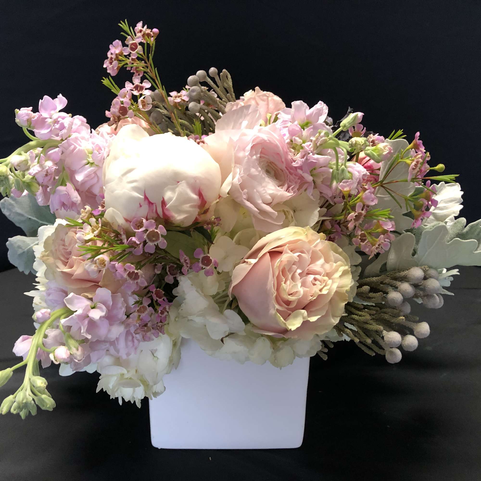 Low pastel arrangement of pink and white roses, peonies, and stock in a white square vase
