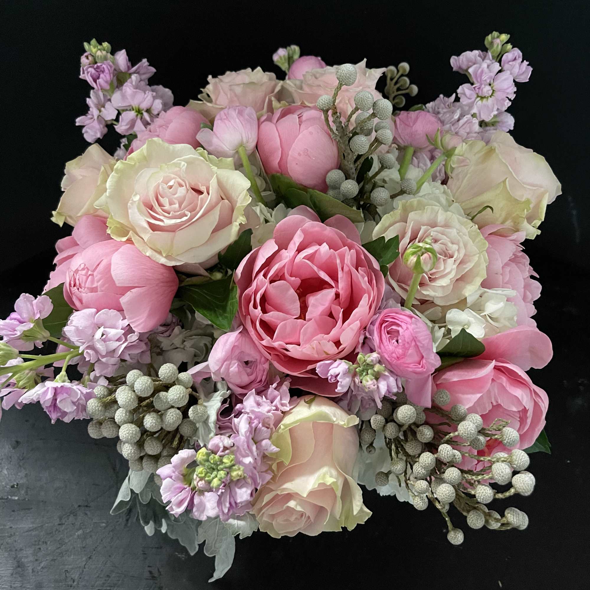 Low arrangement of pink peonies, roses, ranunculus and lavender blooms in a compact mound.