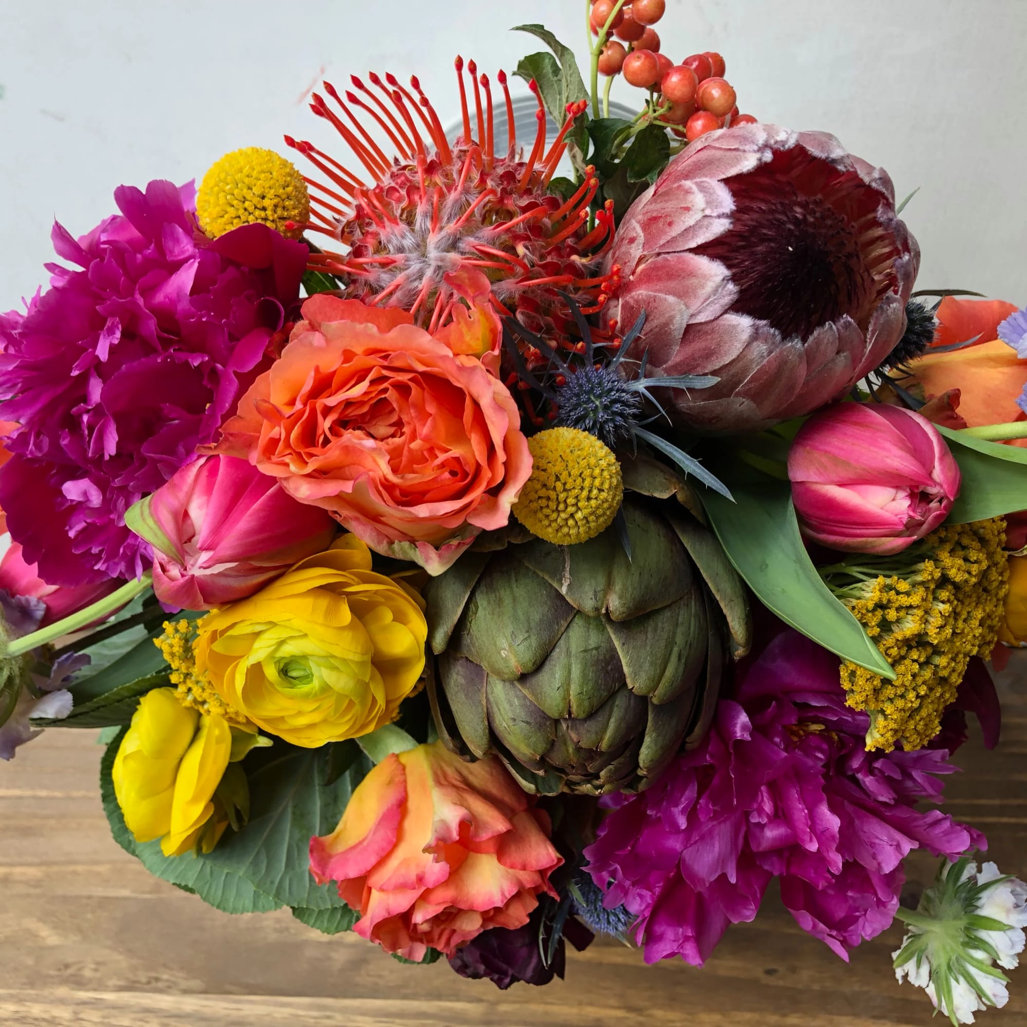 Vibrant mixed arrangement with protea, roses, tulips, and ranunculus in bright pink, orange, and yellow tones