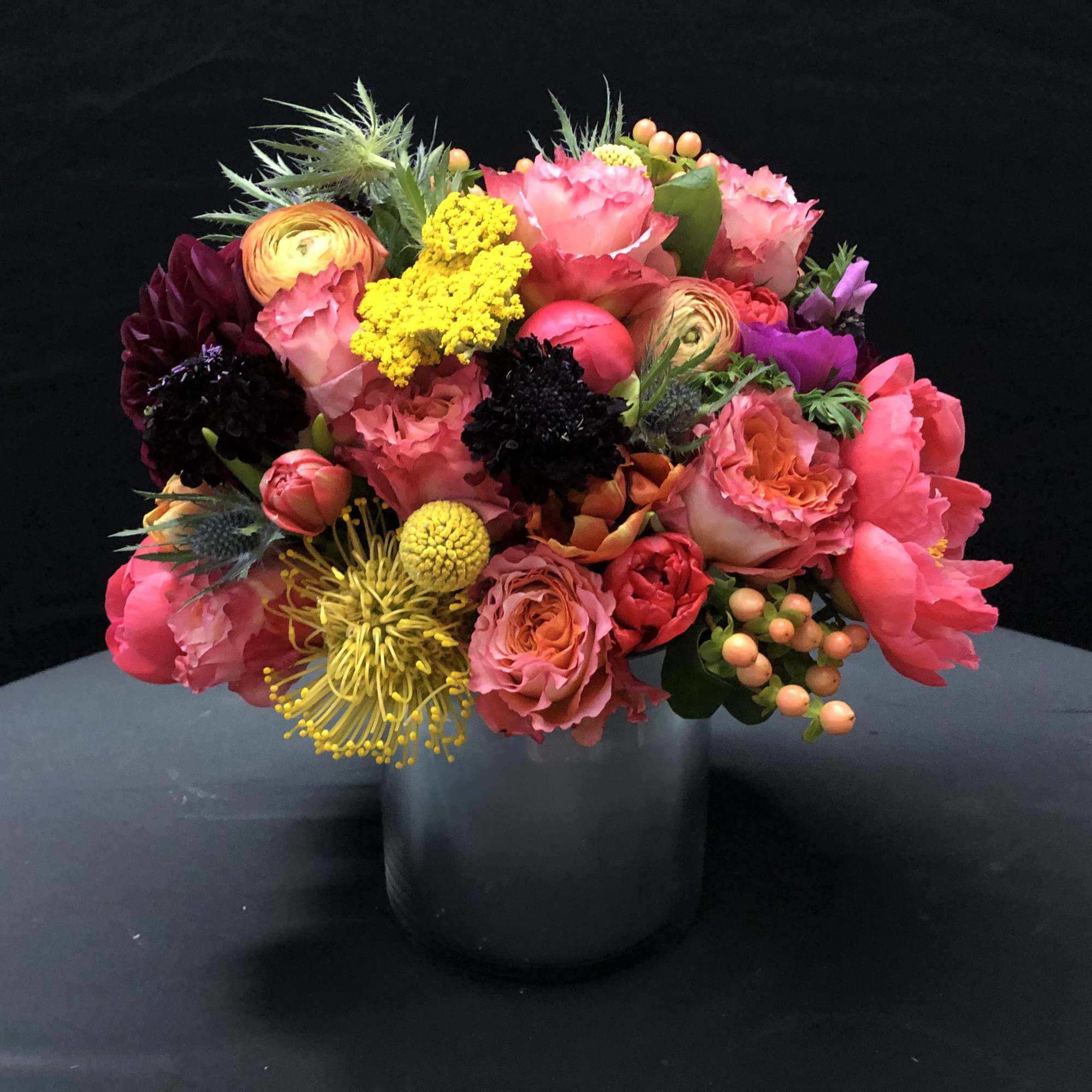 Bright mixed arrangement of pink and orange blooms with yellow accents in a silver cylinder vase