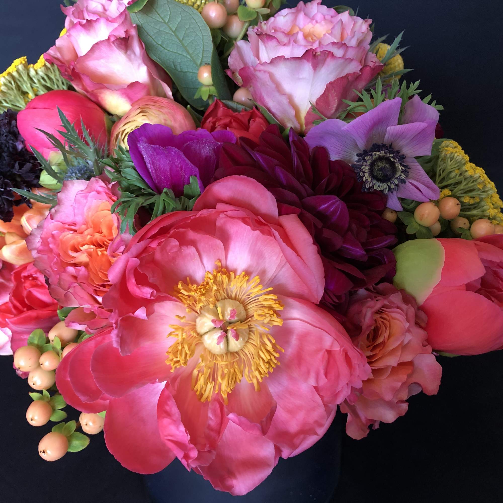 Bright mixed bouquet of pink peonies, roses, and other flowers in a black vase