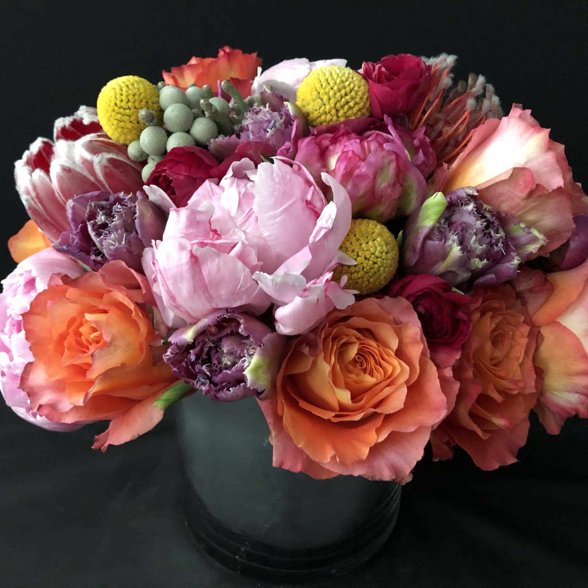 Bright arrangement of pink peonies, orange roses, and mixed blooms in a black round vase